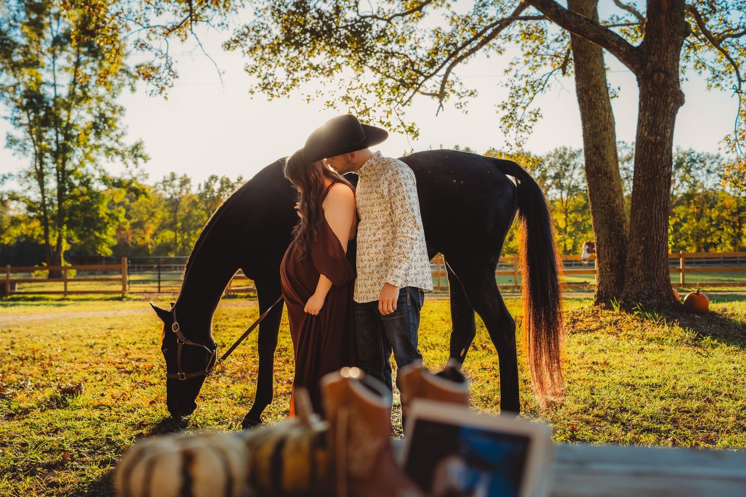 Couple sharing a kiss beside a black horse grazing under large oak tree at golden hour.Charleston South Carolina