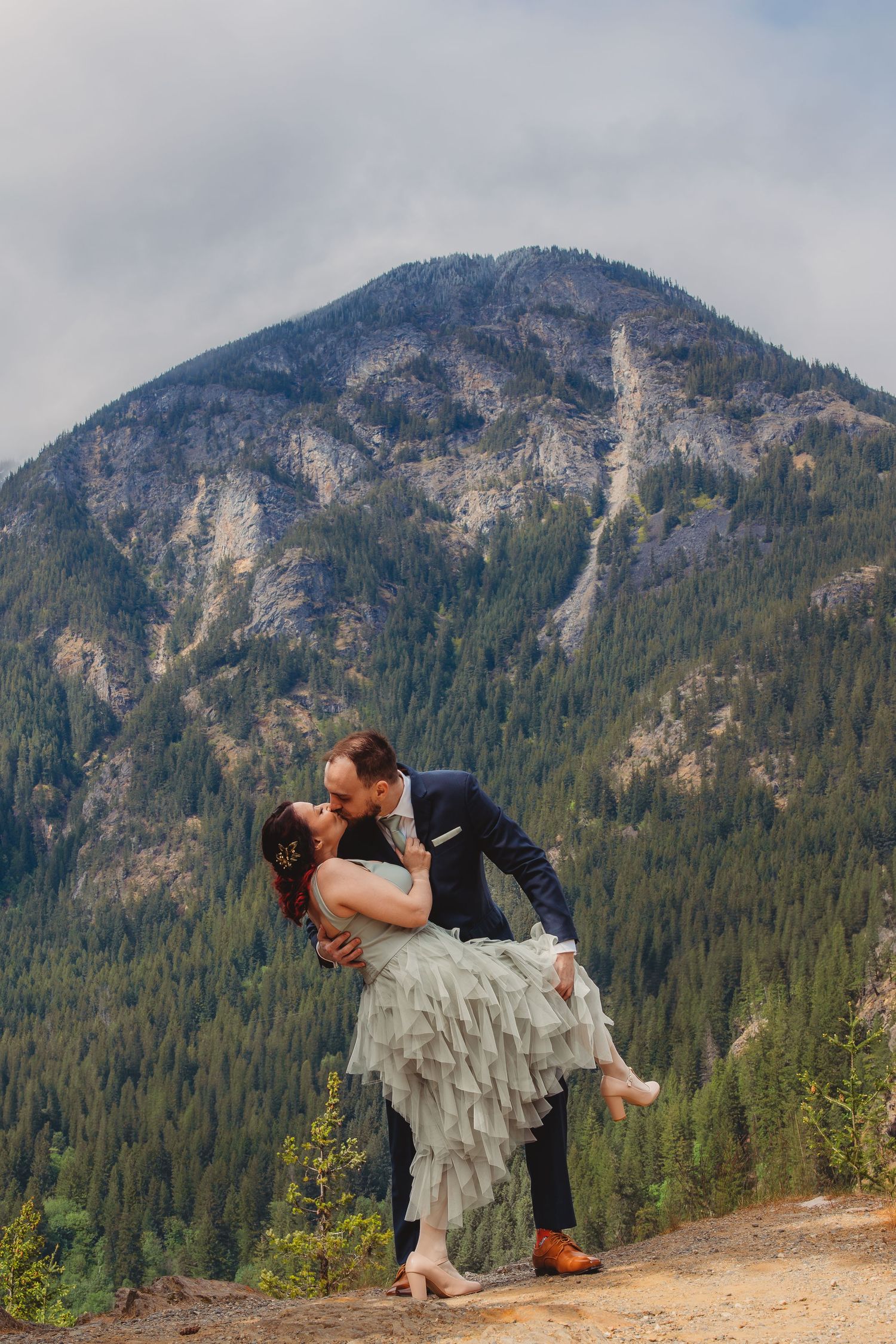 Groom dips bride for a kiss in front of a stunning mountain backdrop during an outdoor wedding ceremony.