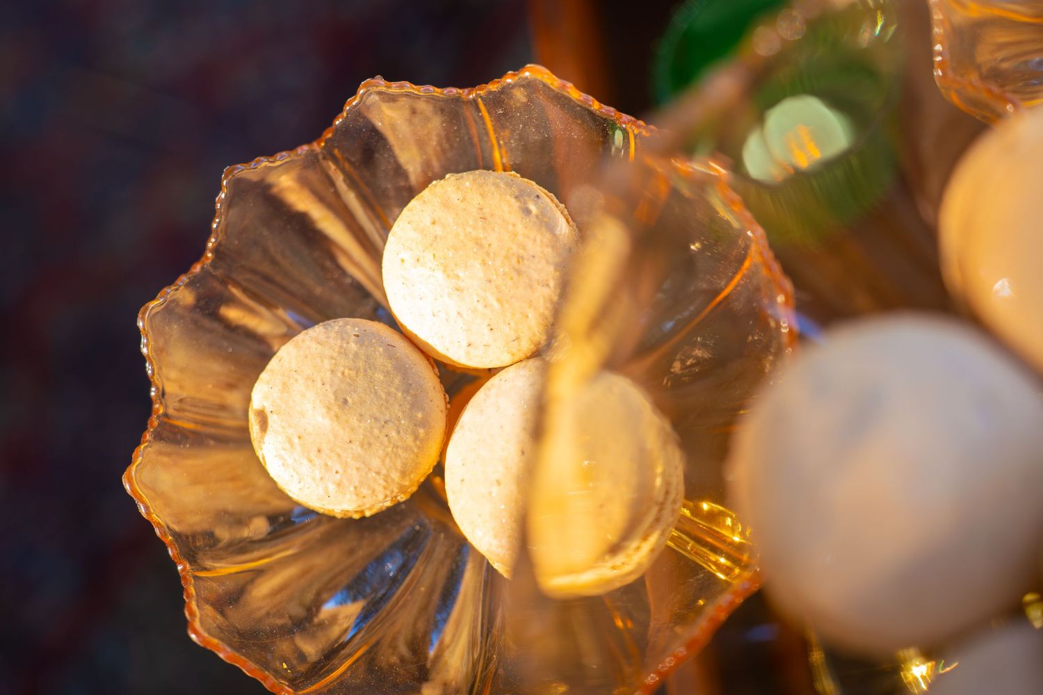 Round white decorative spheres resting in a clear, ruffled glass bowl with warm golden light and blurred festive lights in the background.