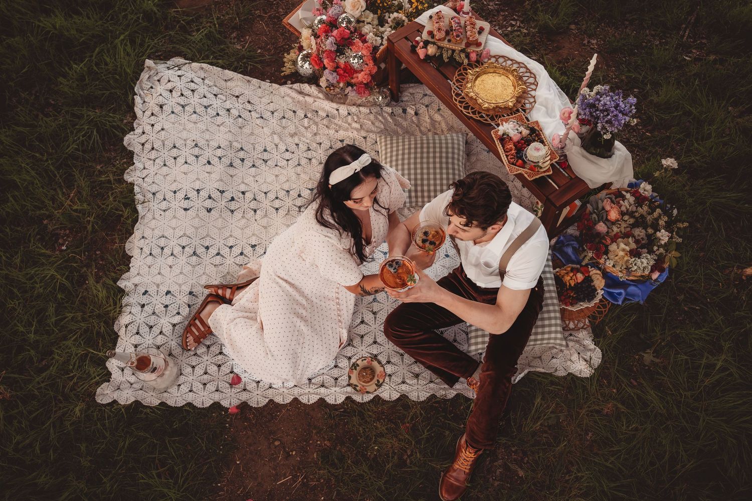 Aerial view of a romantic couple sharing a picnic on a crochet blanket surrounded by flowers.