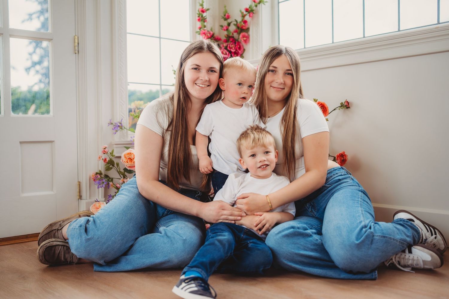 Two young women sitting on floor smiling with two toddlers in bright floral room.Summerville South Carolina