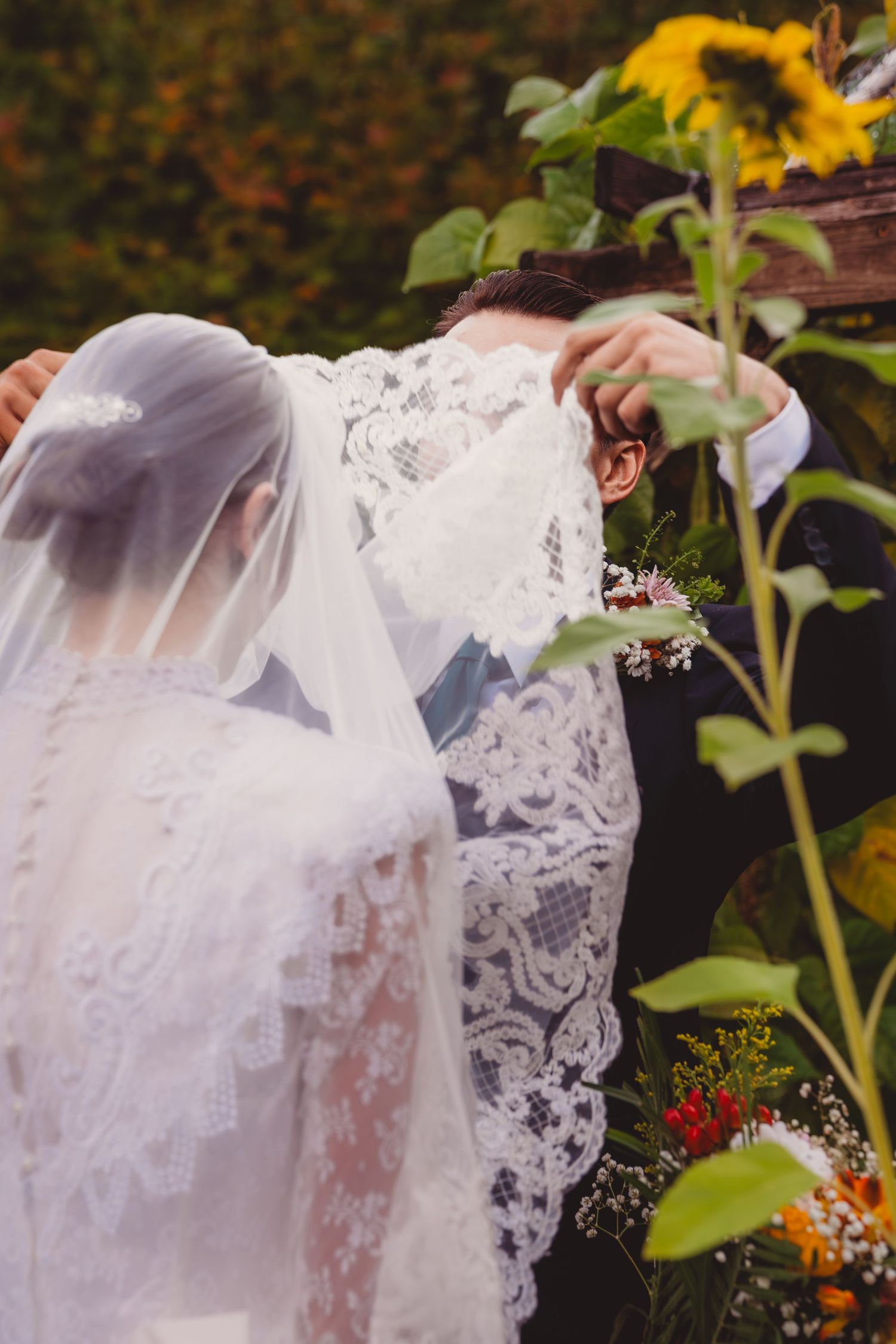 Bride and groom sharing a kiss under a floral arch with sunflowers at an outdoor wedding ceremony.