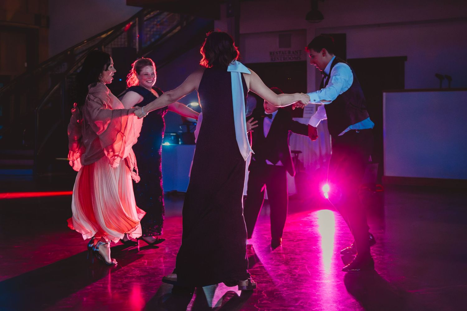 Couples dancing elegantly on a colorful lit dance floor at a formal evening event.