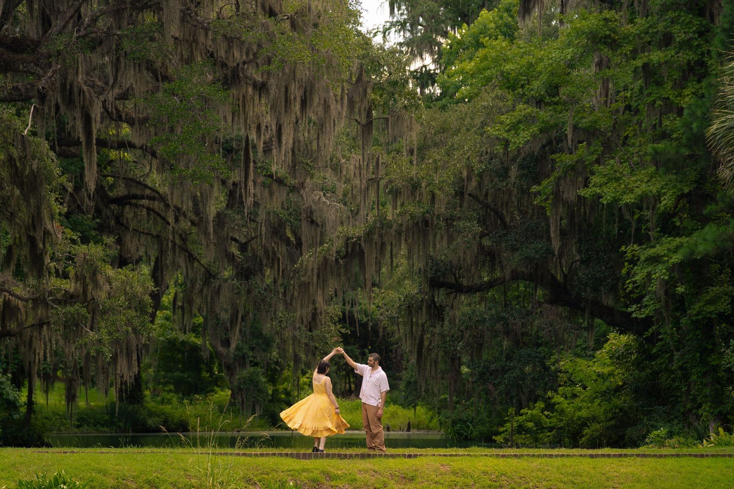 Couple dancing under Spanish moss-draped trees in a lush green Southern garden, woman in yellow dress.