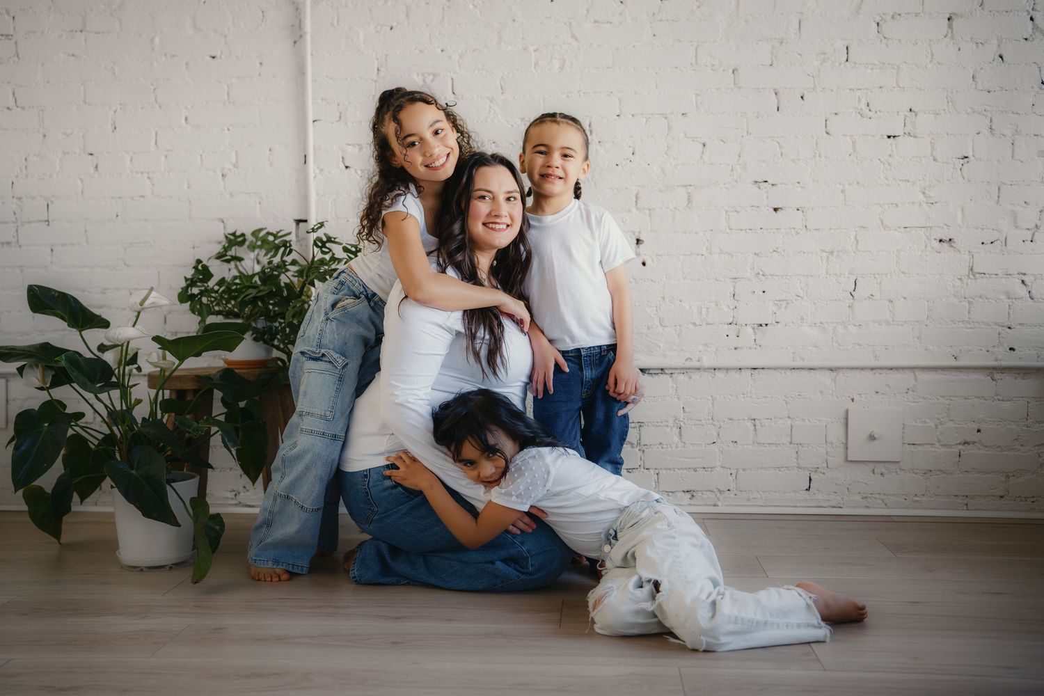 Smiling mother sitting on floor with three children hugging her in bright white room.Summerville South Carolina