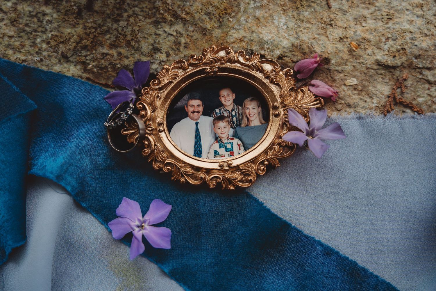 Gold ornate locket with family photo surrounded by purple flowers on blue ribbon fabric.