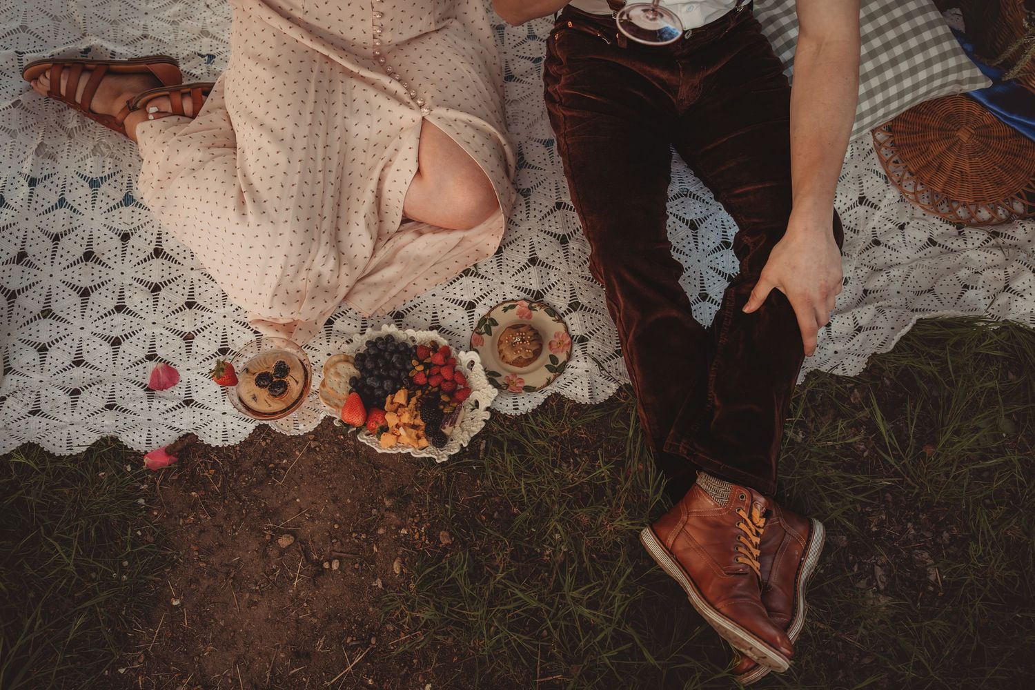 Couple enjoying a boho picnic on a white quilt with fresh fruit and tarts on a sunny day outdoors.
