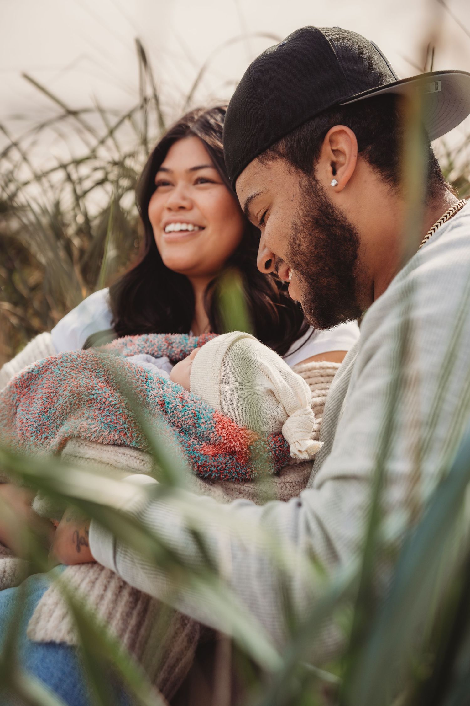 Happy couple holding their newborn baby outdoors among tall grass.