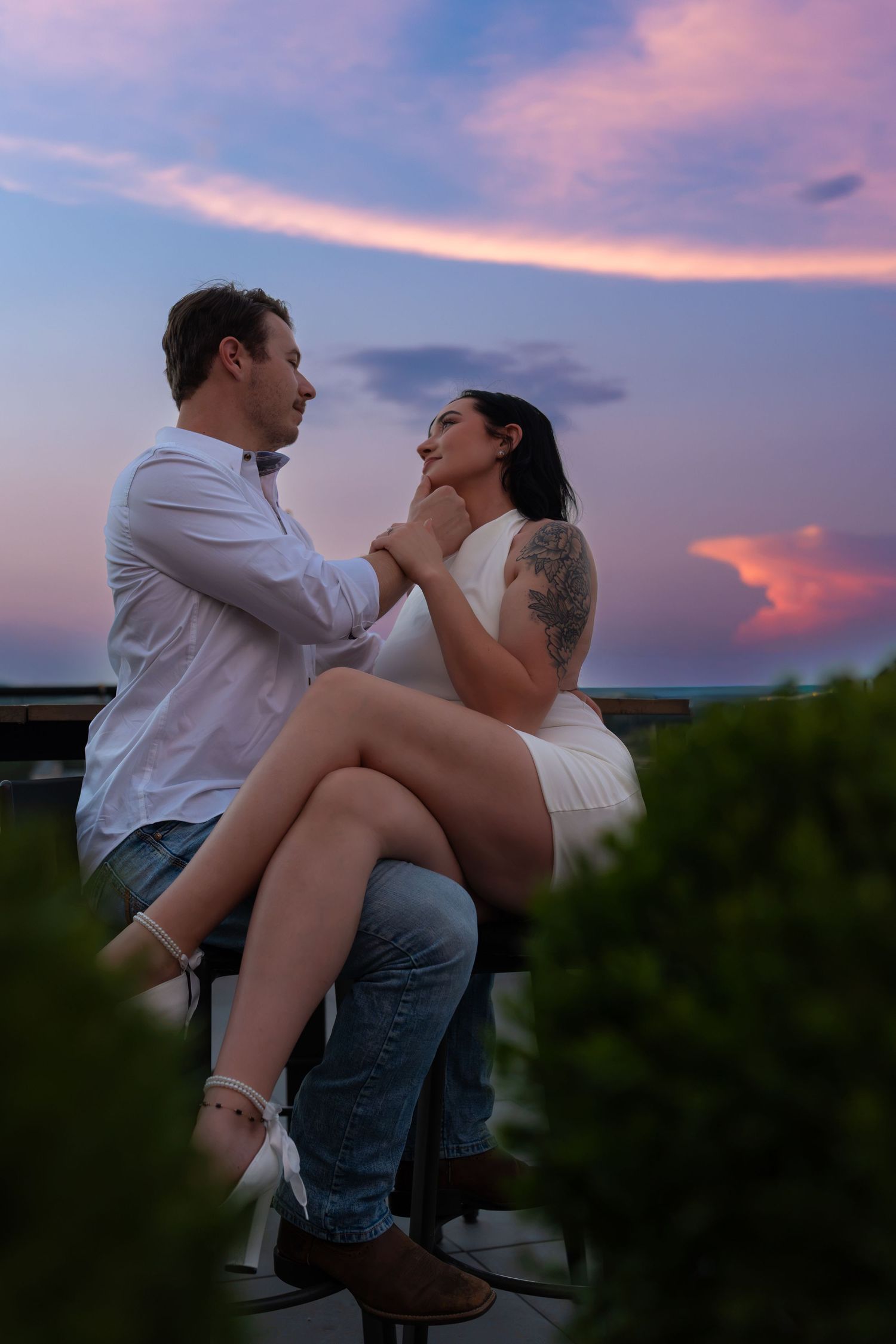 Couple sharing an intimate moment on a rooftop terrace as a vivid pink and purple sunset glows behind them.