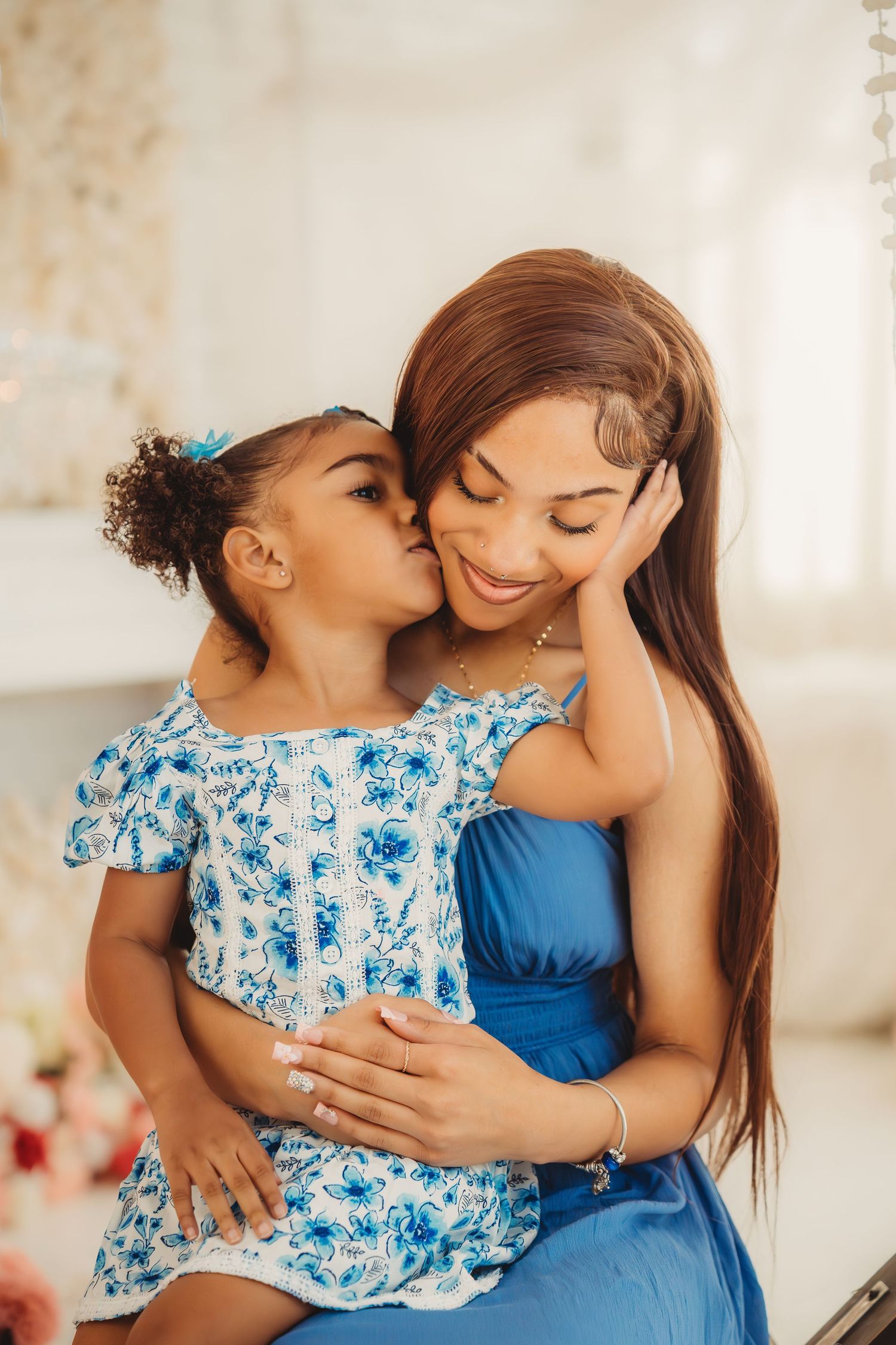 Young girl in floral dress lovingly kissing smiling mother in blue dress indoors.Summerville South Carolina
