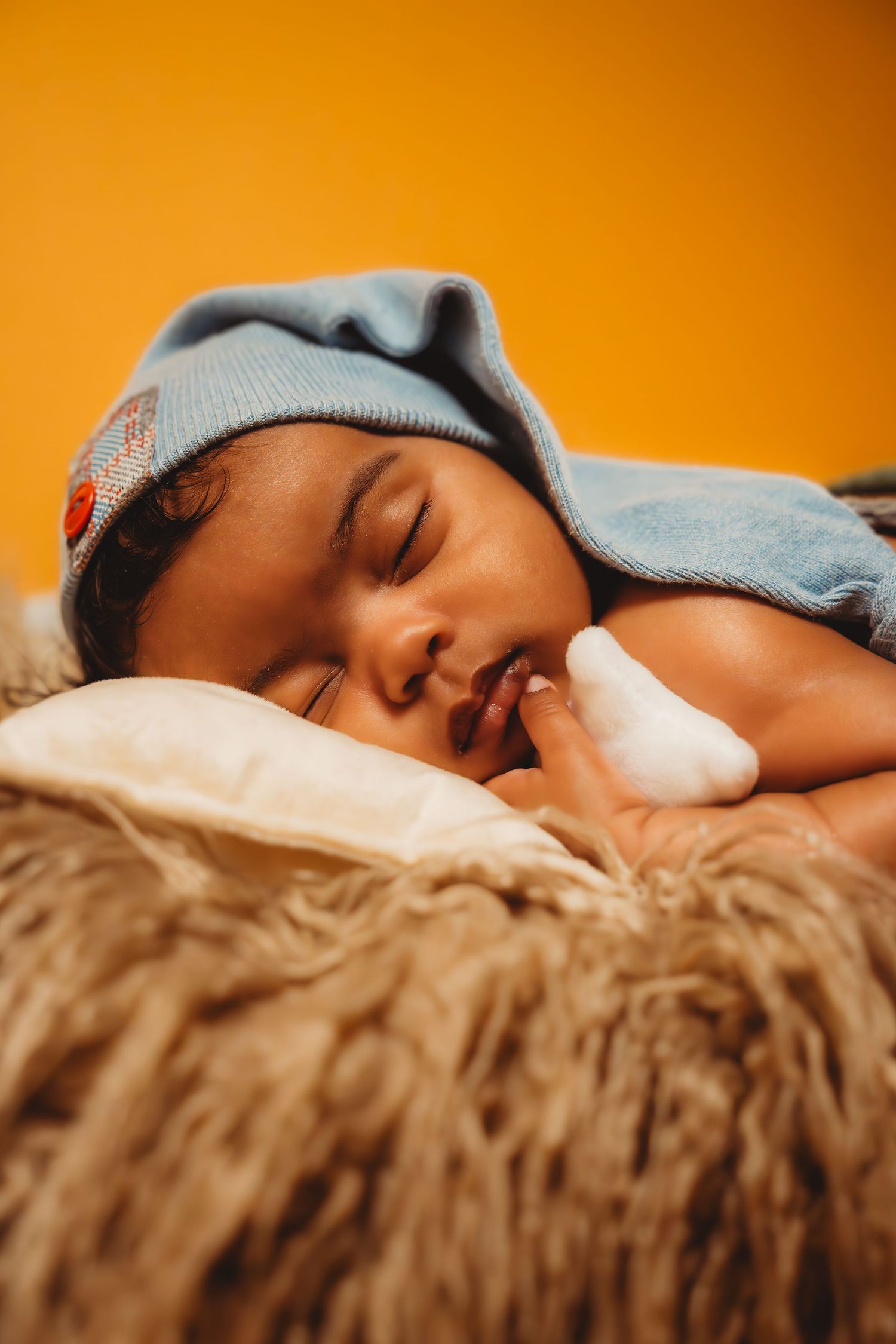 Peaceful newborn baby sleeping in blue knit hat on fluffy blanket.