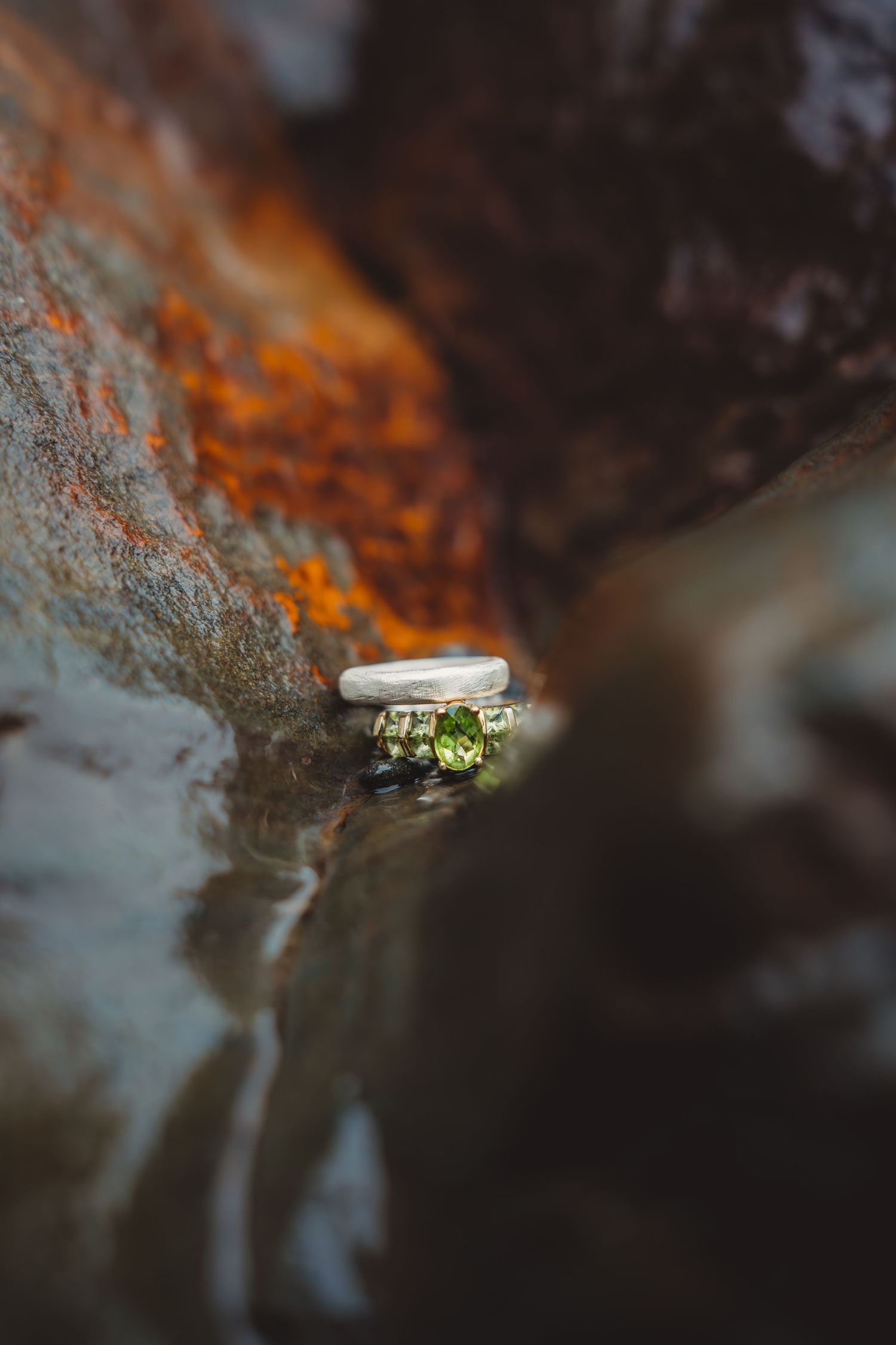 Silver wedding ring set featuring a green peridot gemstone resting on a rustic textured surface. Oregon