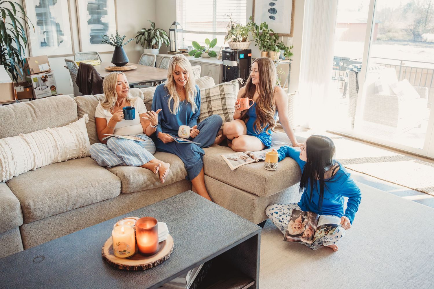 Two women and children in pajamas relaxing on a cozy living room couch, enjoying morning coffee together.
