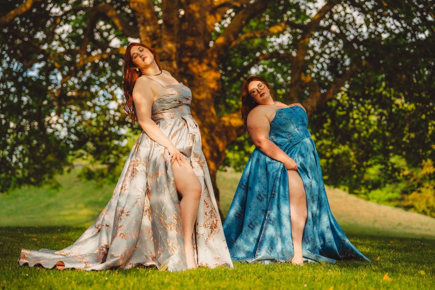 Two women in flowing floral and blue gowns posing gracefully outdoors under a large oak tree. Charleston South Carolina