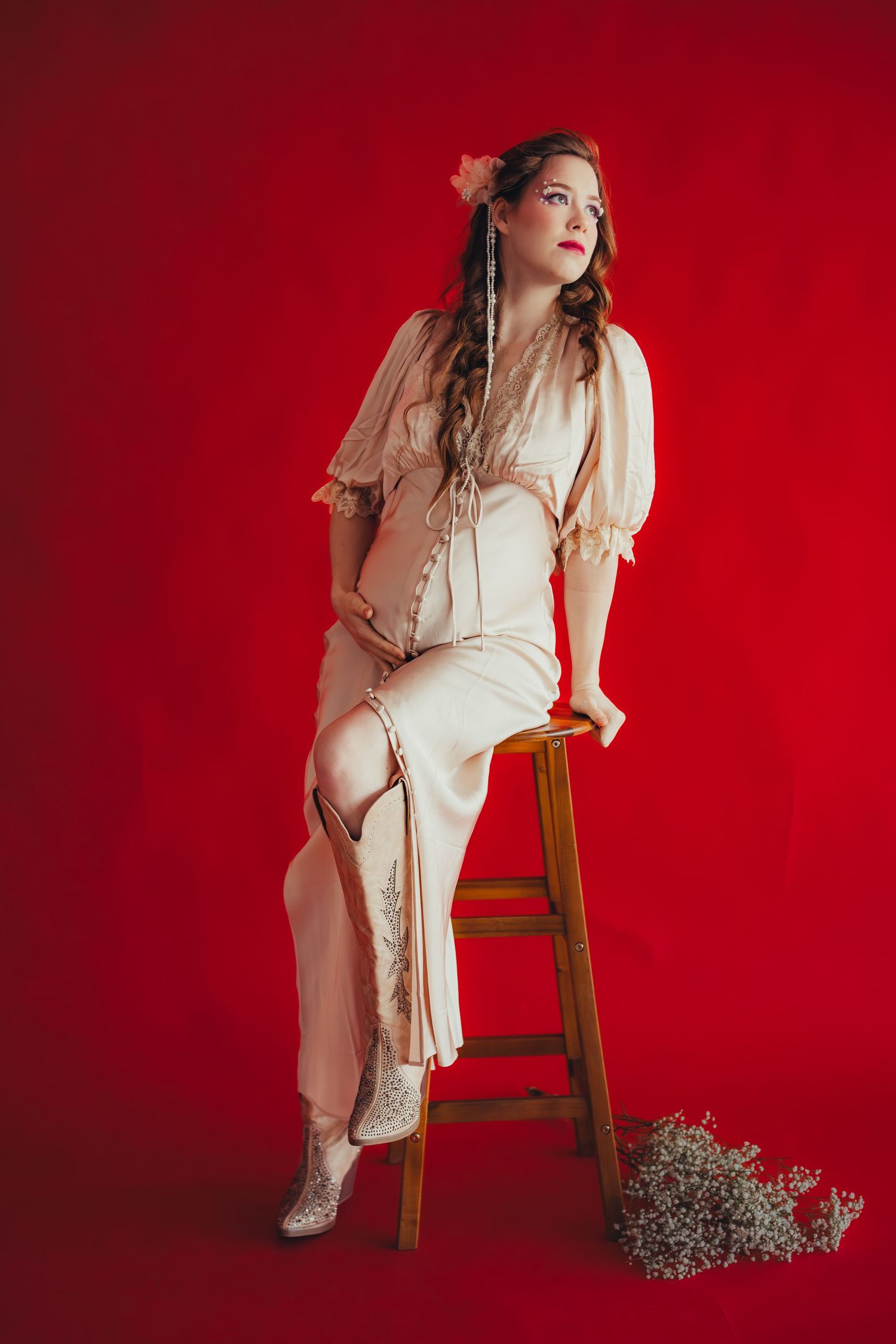 Elegant woman in vintage cream dress seated on wooden stool against vibrant red background.Summerville South Carolina