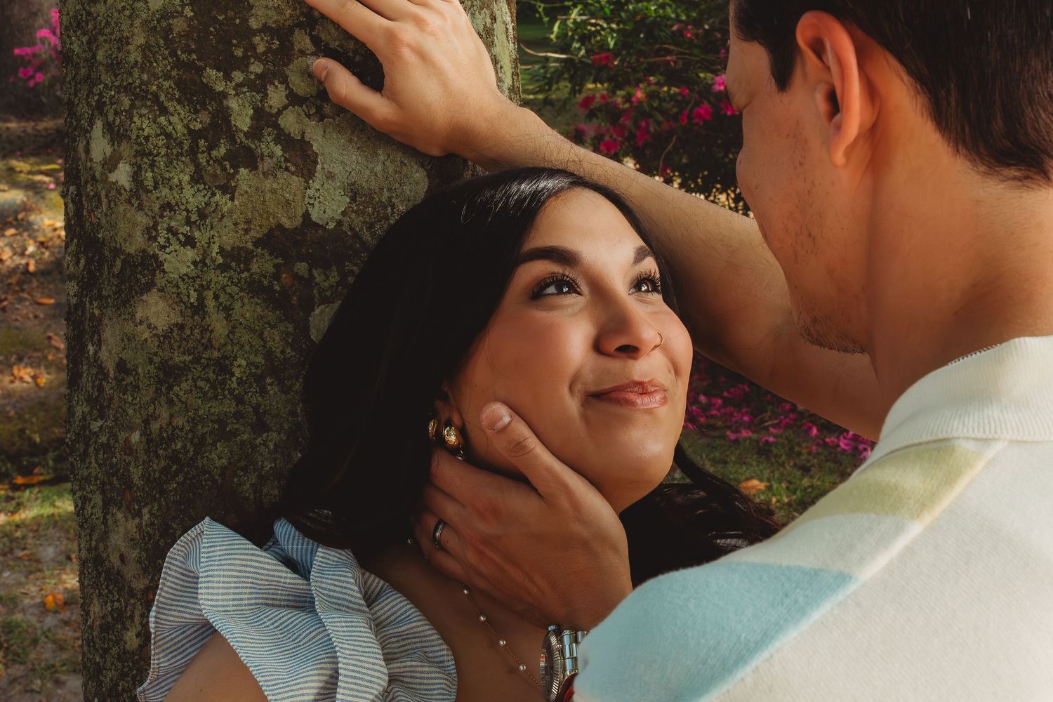 A romantic couple shares a tender moment outdoors, with the man gently holding the woman's face as she smiles up at him.