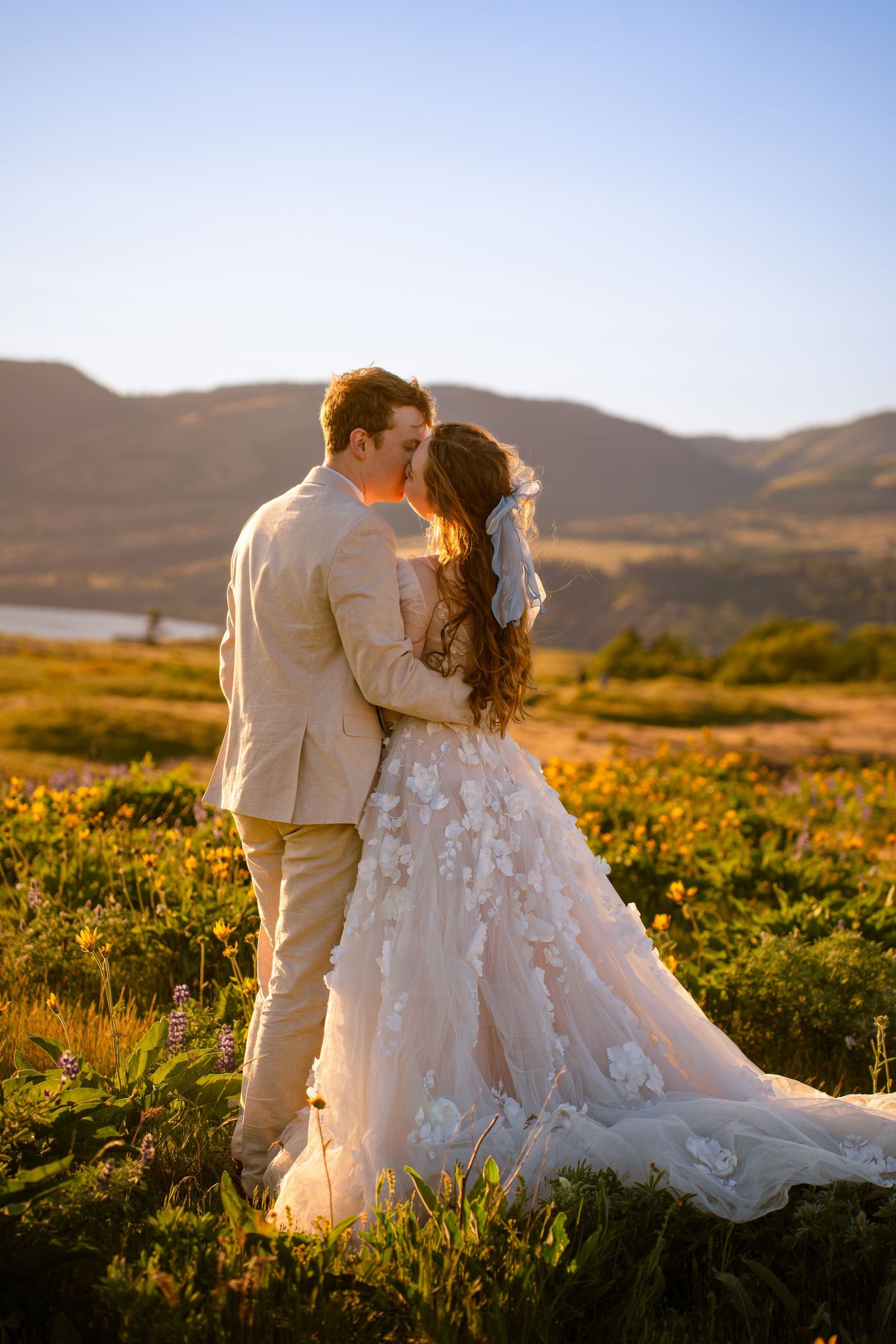 Bride and groom sharing romantic kiss in golden wildflower meadow at sunset.