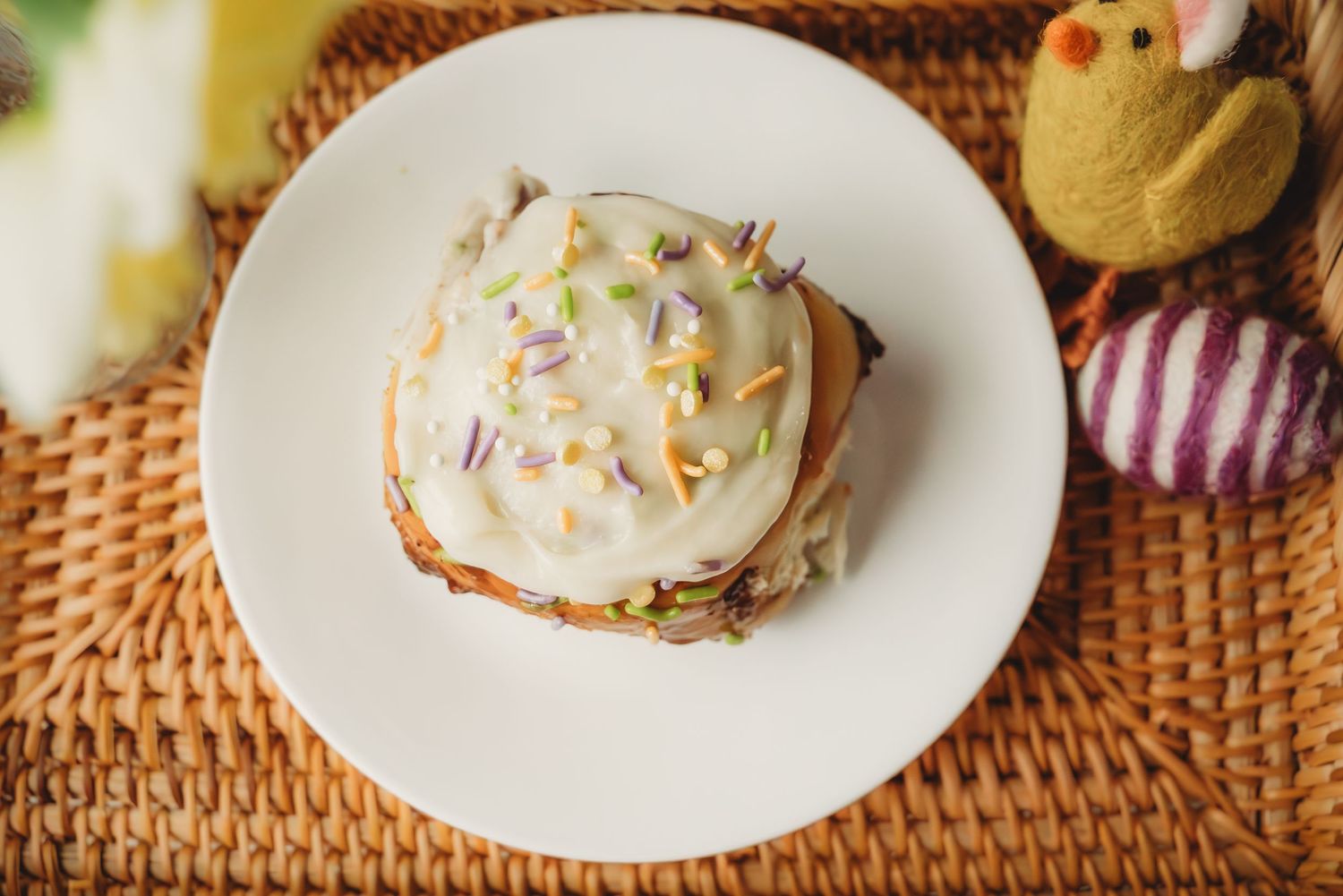 Easter cupcake with white frosting and colorful sprinkles on a white plate with festive decorations.