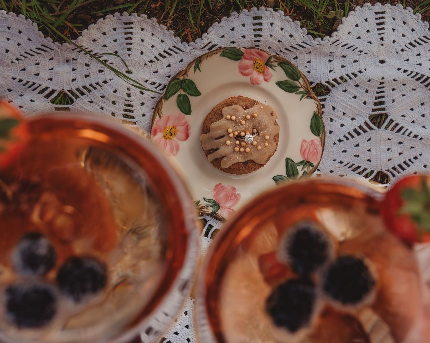 Overhead view of a muffin on floral plate with copper bowls of blackberries on lace tablecloth outdoors.