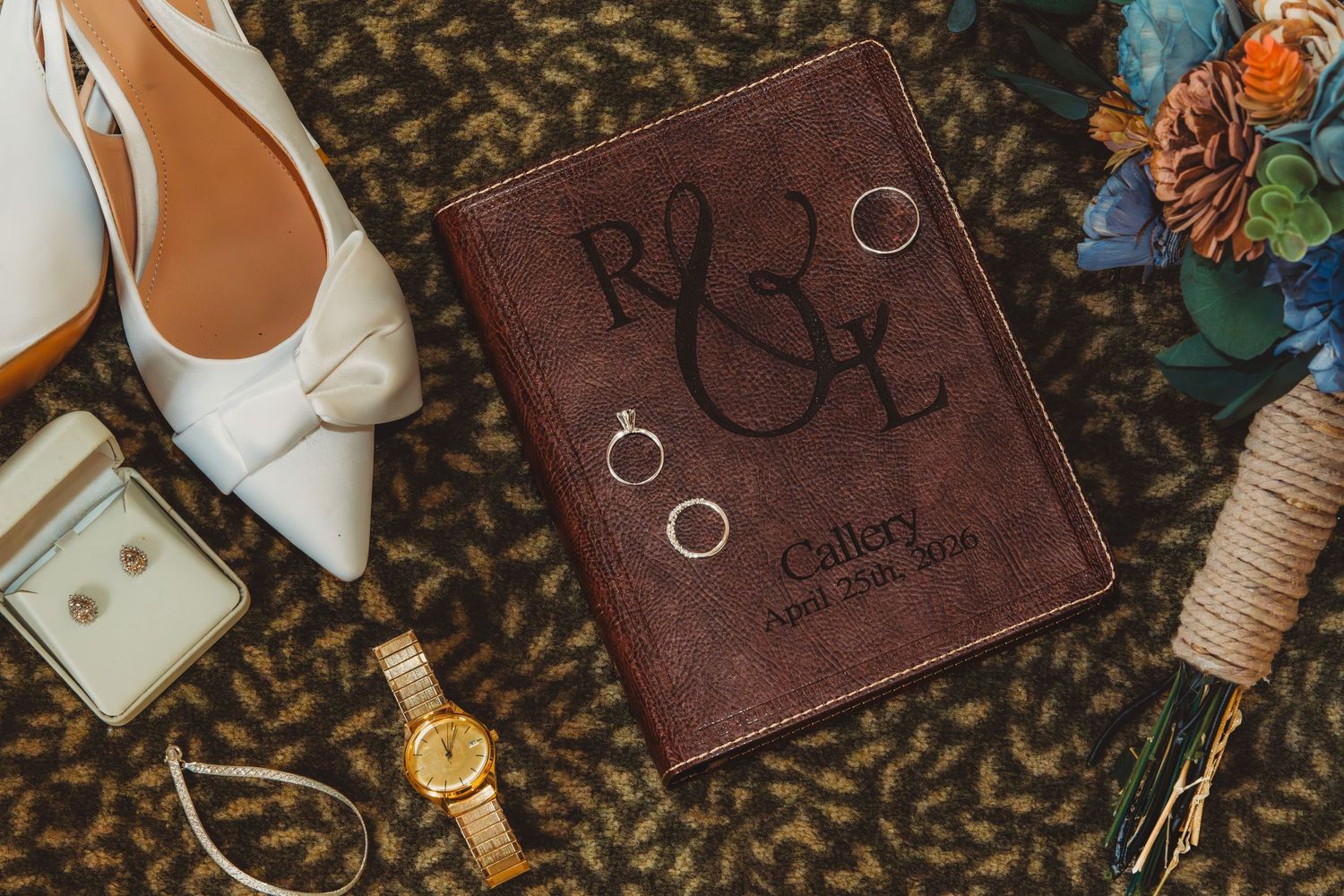 Wedding flat lay featuring leather monogram guest book, rings, white heels, bouquet, and watch. Arkansas