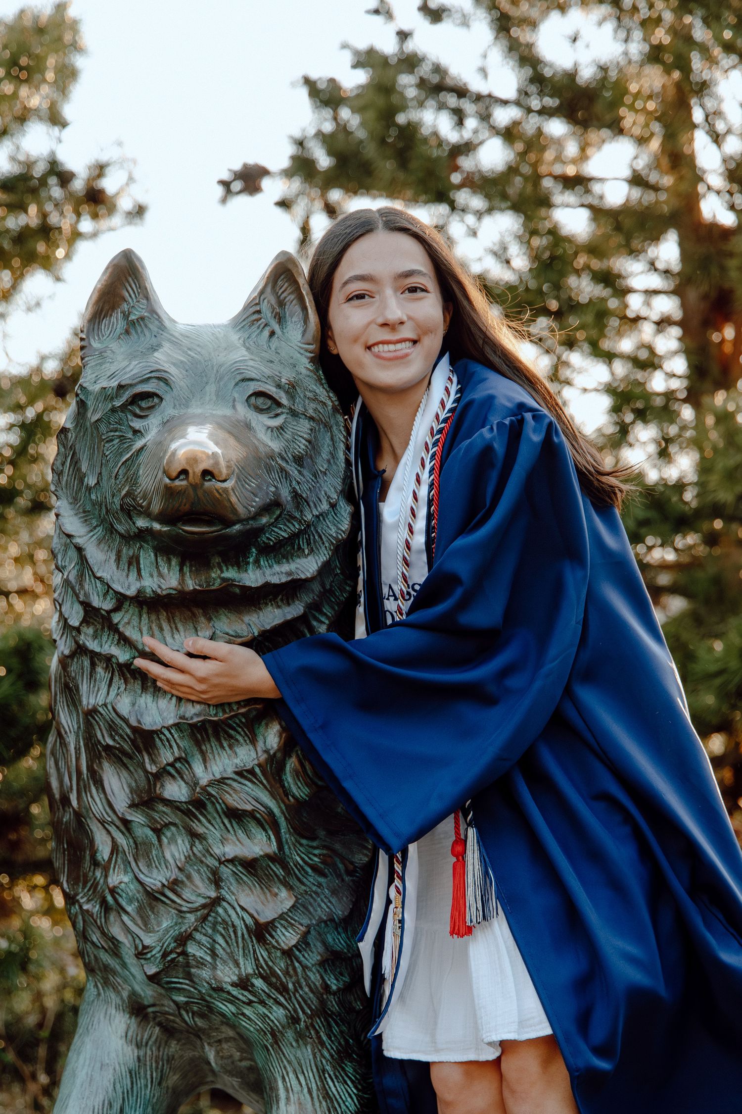 UConn graduation portrait at the Jonathan statue, celebrating Husky pride with a senior in cap and gown surrounded by campus greenery.