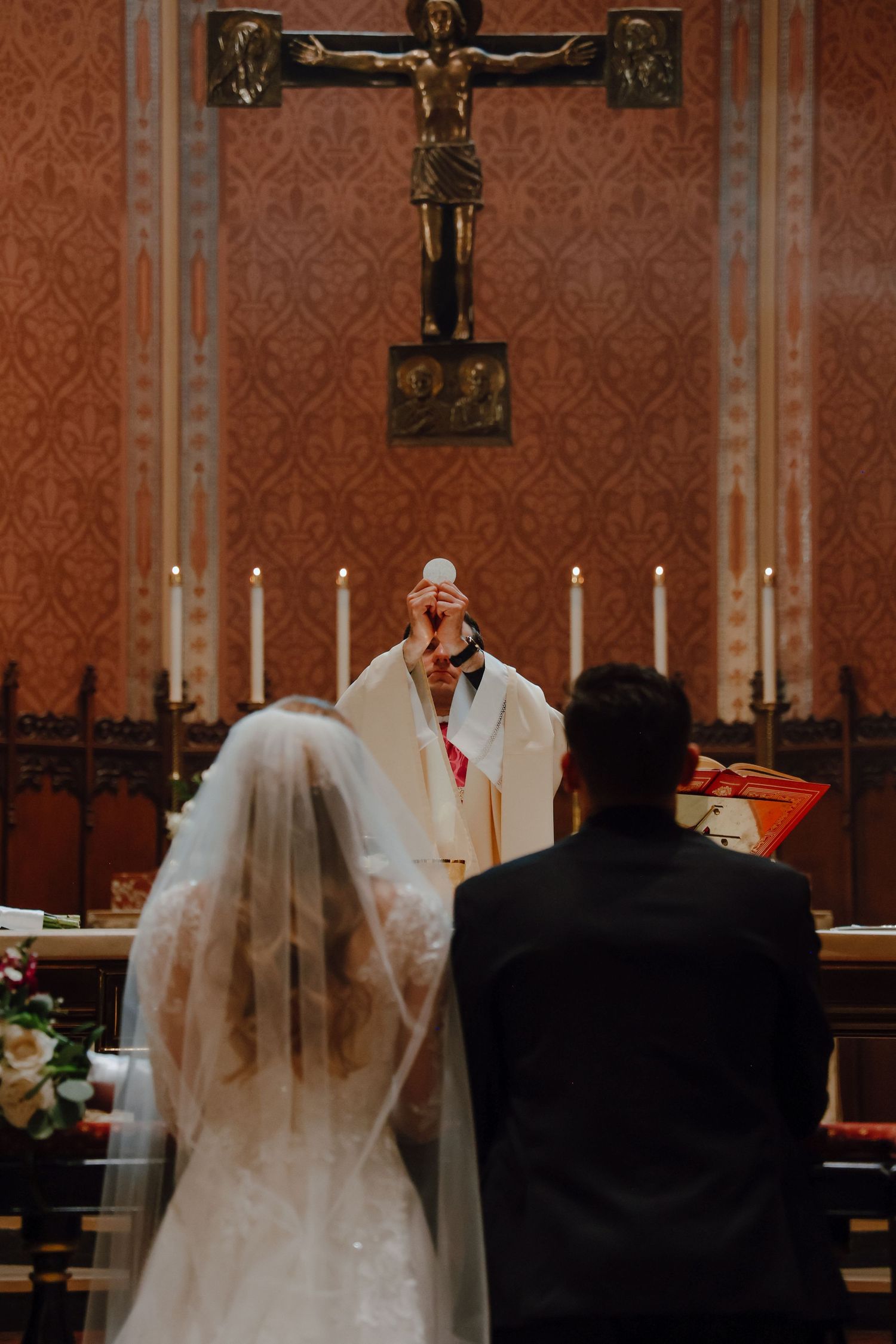 Consecration during a Nuptial Mass, as the priest elevates the Host and the couple witnesses Christ’s presence at their wedding feast.
