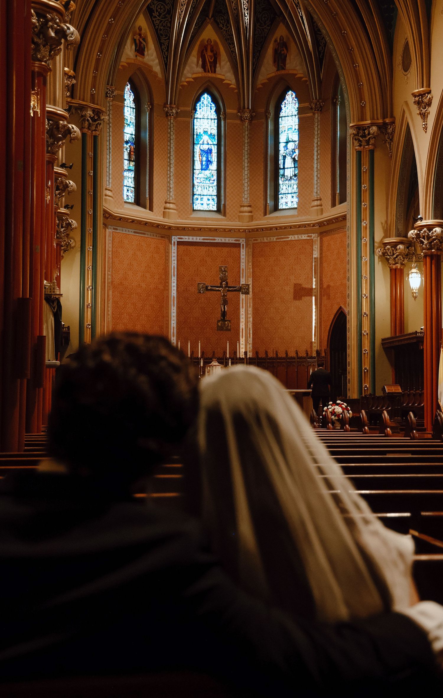 Catholic wedding at St. Mary’s New Haven, captured in warm light as the couple prays beneath ornate architecture and the central crucifix.