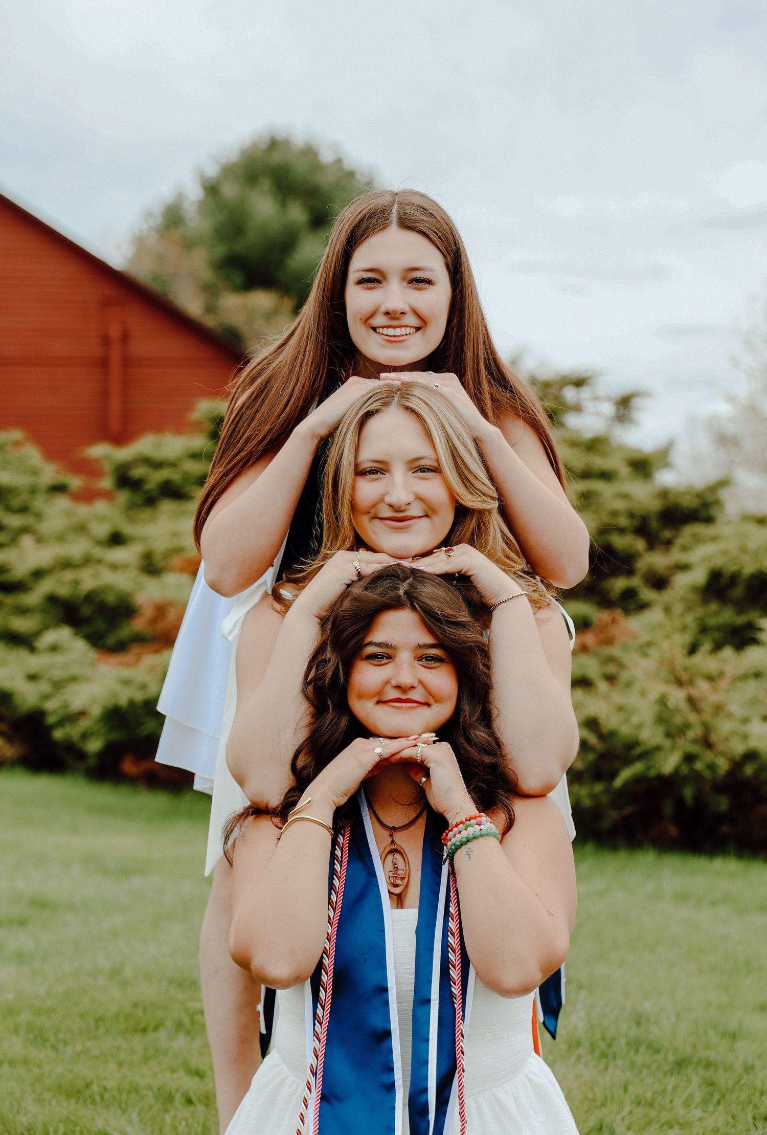 Joyful outdoor graduation portrait with friends stacked playfully, celebrating achievement in bright summer light and greenery.