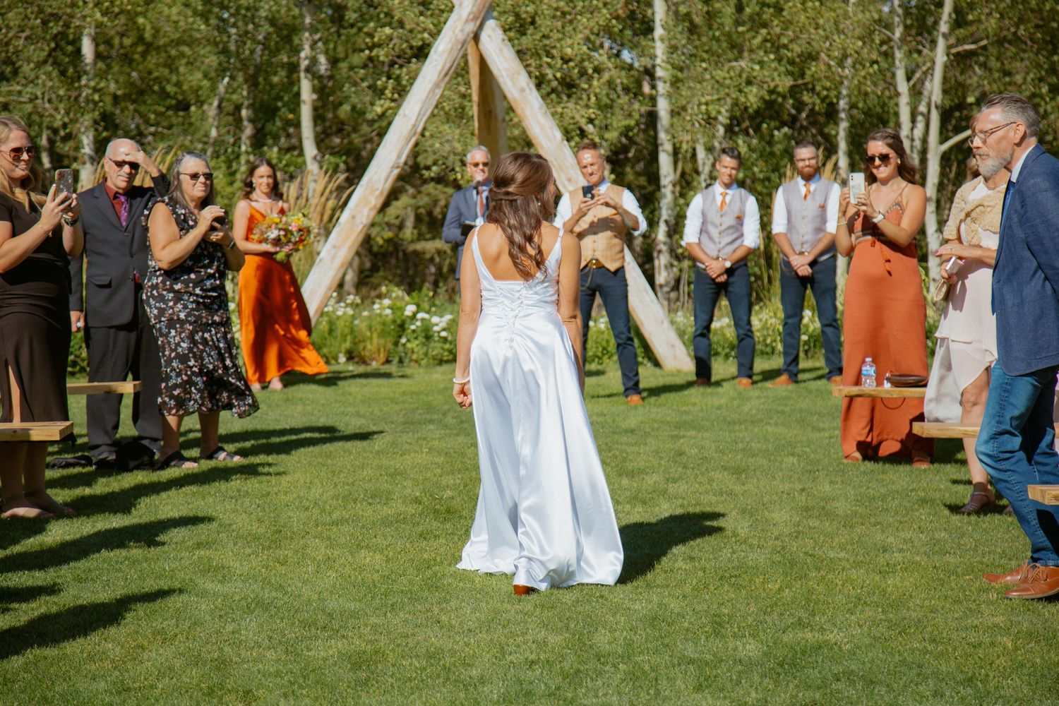 Wedding guests gather outdoors in a scenic grassy area with aspen trees for a rustic ceremony.