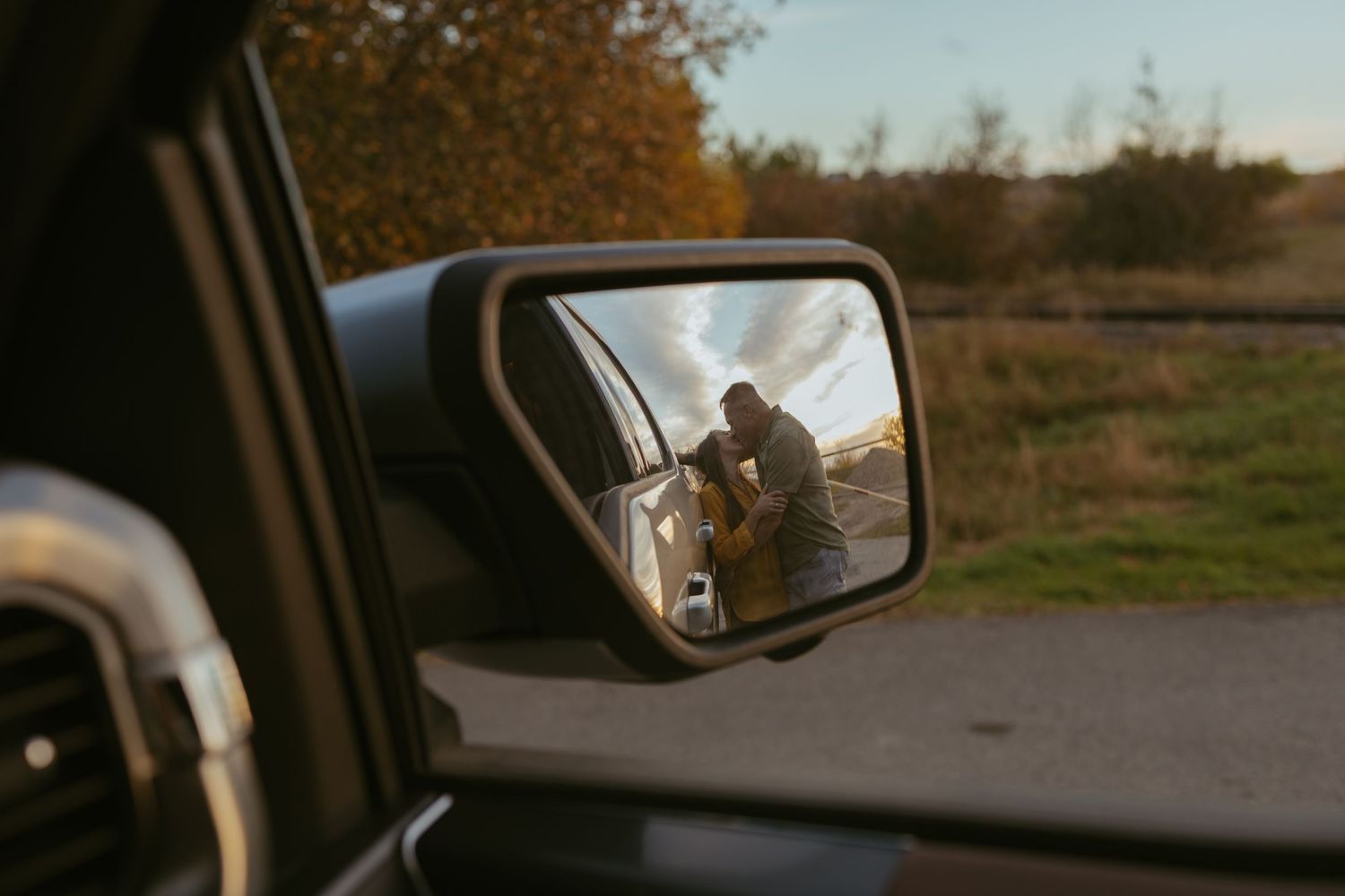 Car side mirror reflection capturing a scenic rural landscape at sunset.