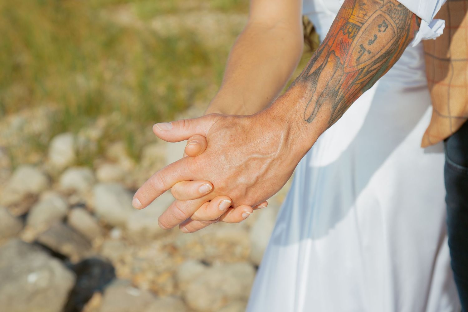 Close-up of tattooed arm and hands against white wedding dress.