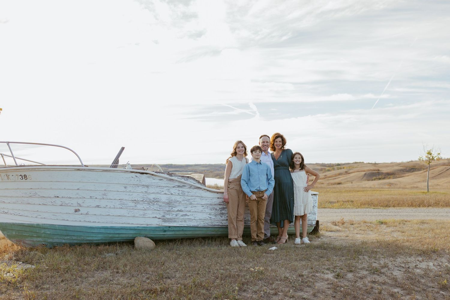 People gathered near an old boat on a grassy hillside overlooking a serene lake.