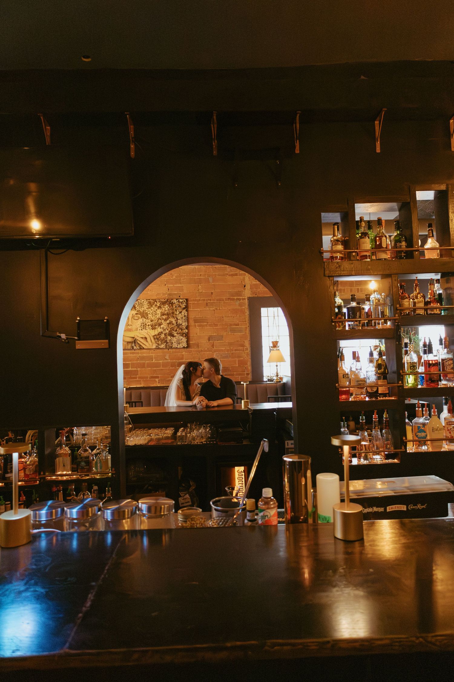 A dimly lit bar interior with wooden accents and bottles displayed on shelves.