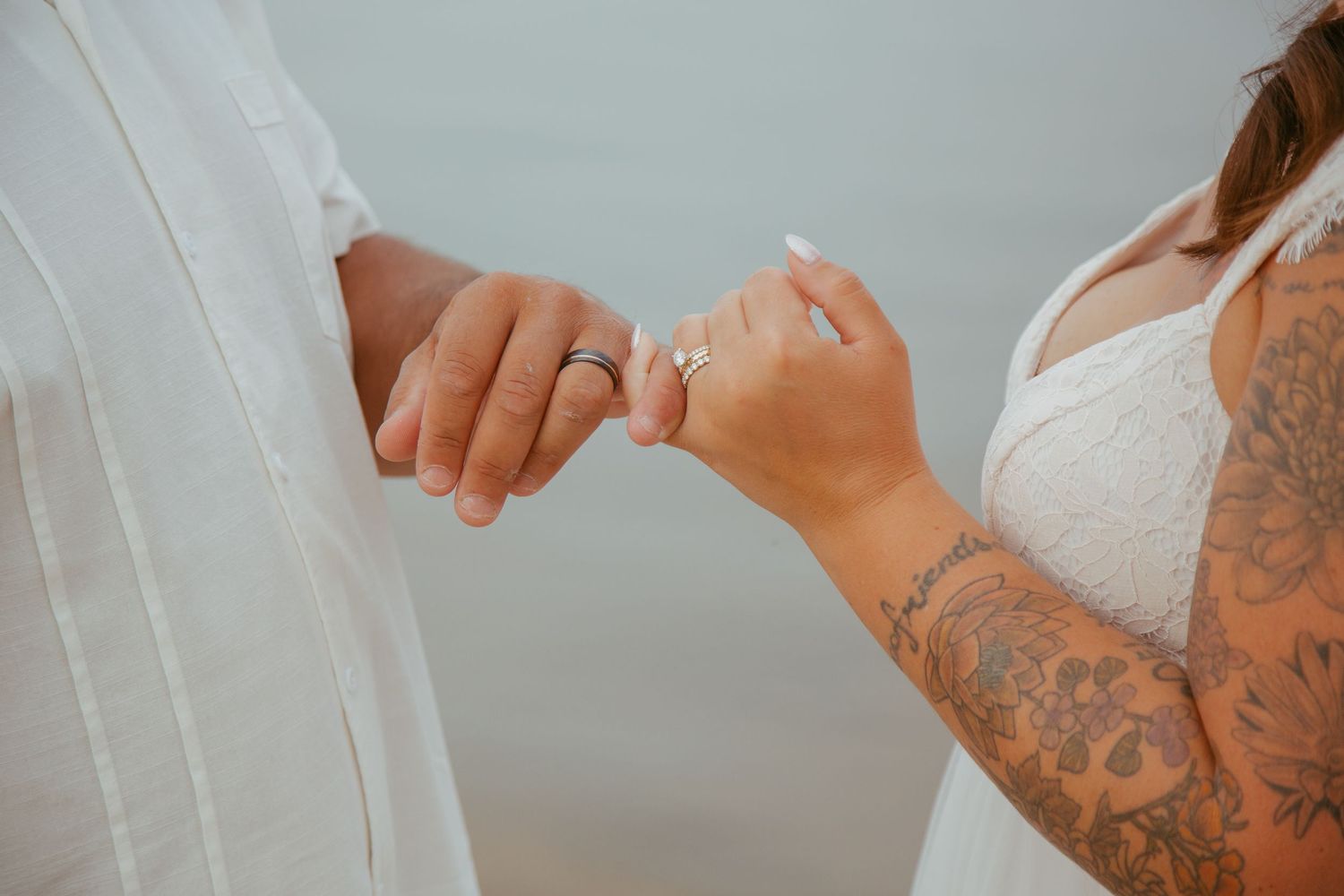 Close up of tattooed hands making pinky promise against white fabric background.