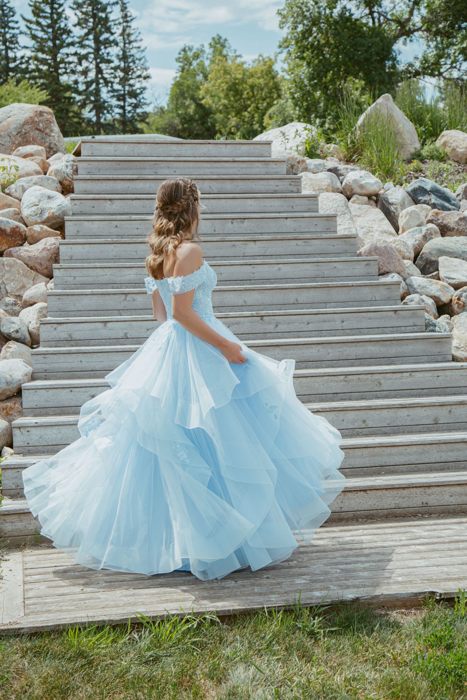 A light blue ballgown cascades down concrete steps surrounded by decorative rocks and greenery.