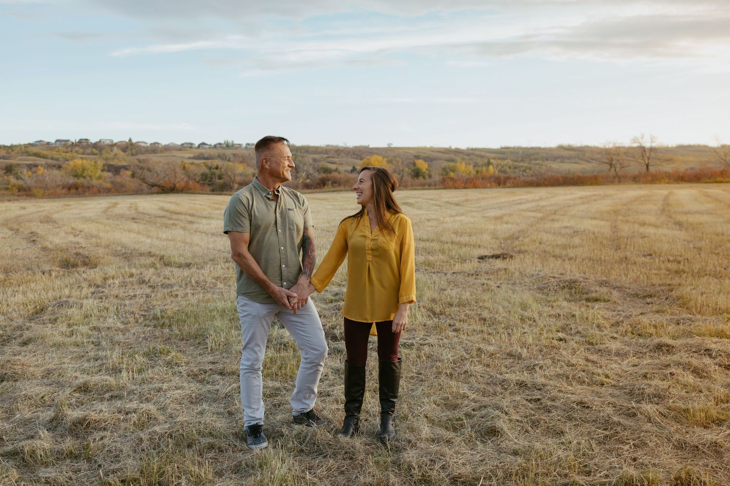 Two people stroll together across a vast open field at sunset.