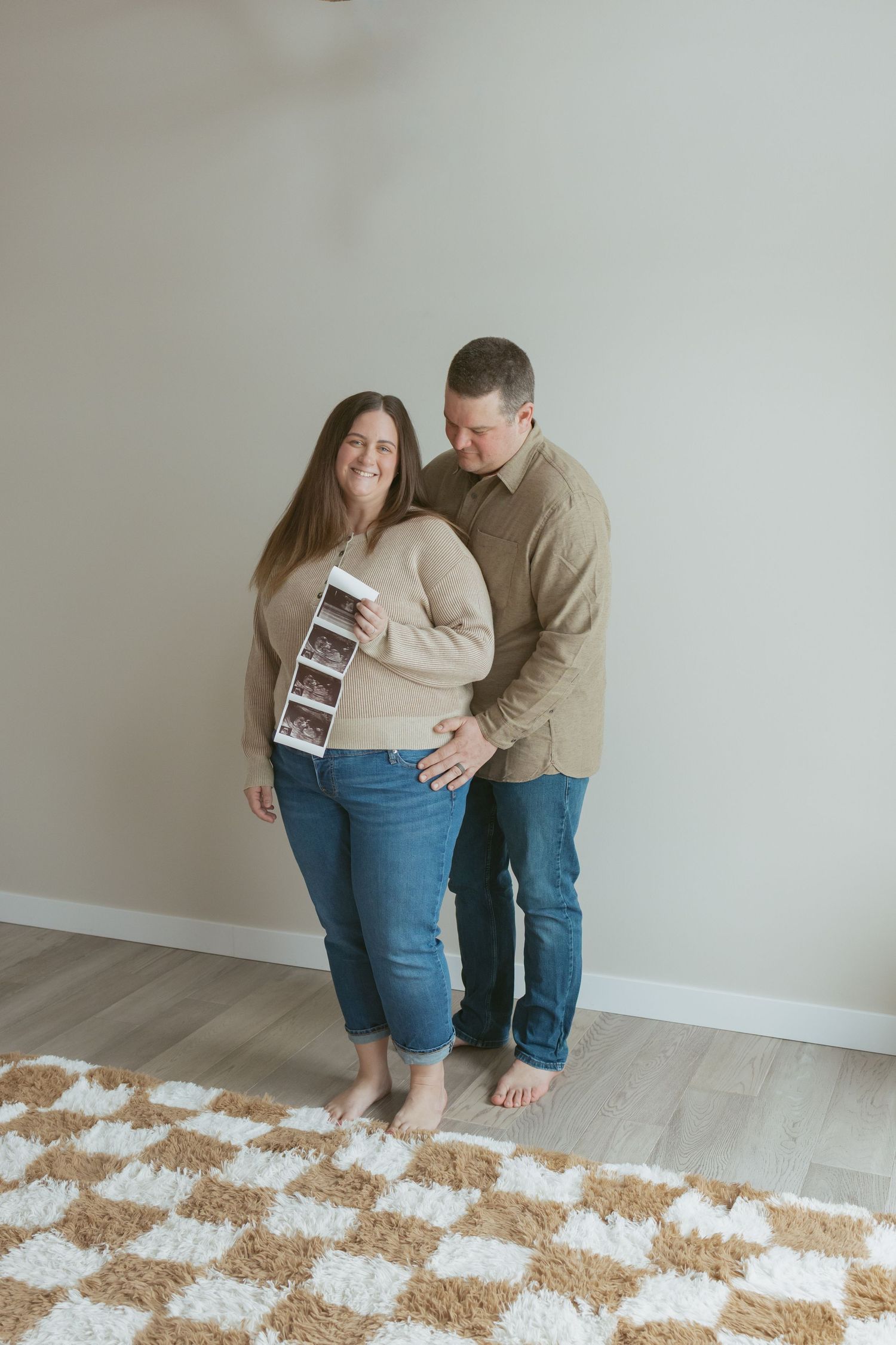 Happy couple holding ultrasound photos, announcing pregnancy, standing together in a cozy room with neutral tones.