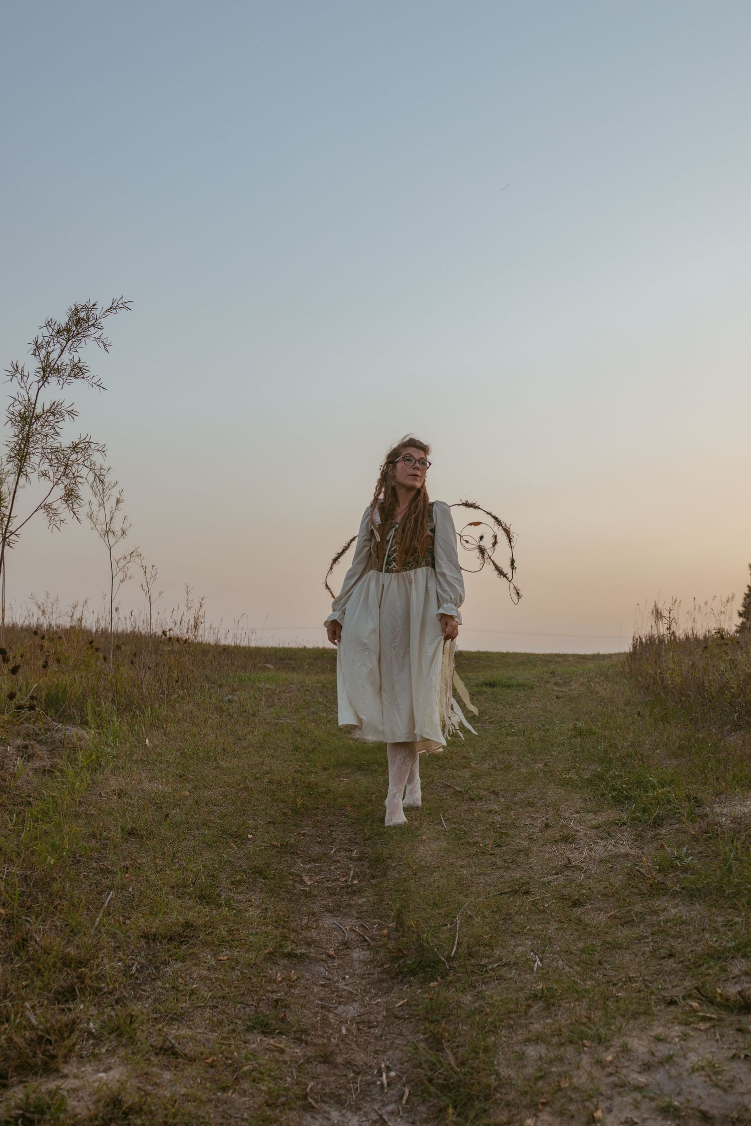 A figure in white walking along a grassy hilltop at dusk.