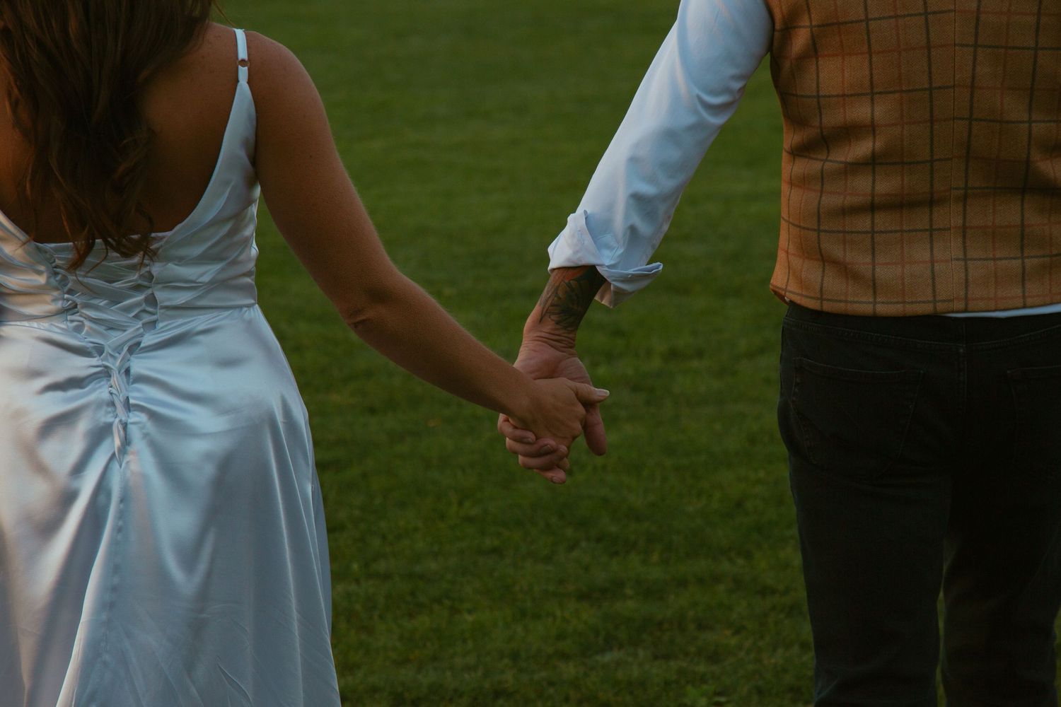 Close-up details of formal attire and joined hands during an outdoor celebration.