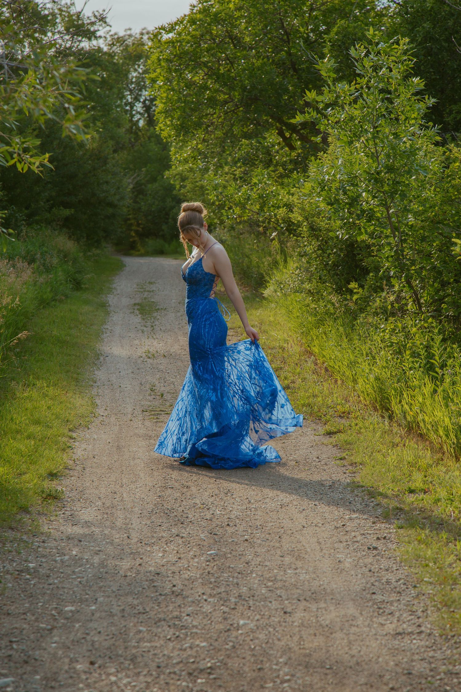 Person in blue formal dress walking along a gravel nature path.