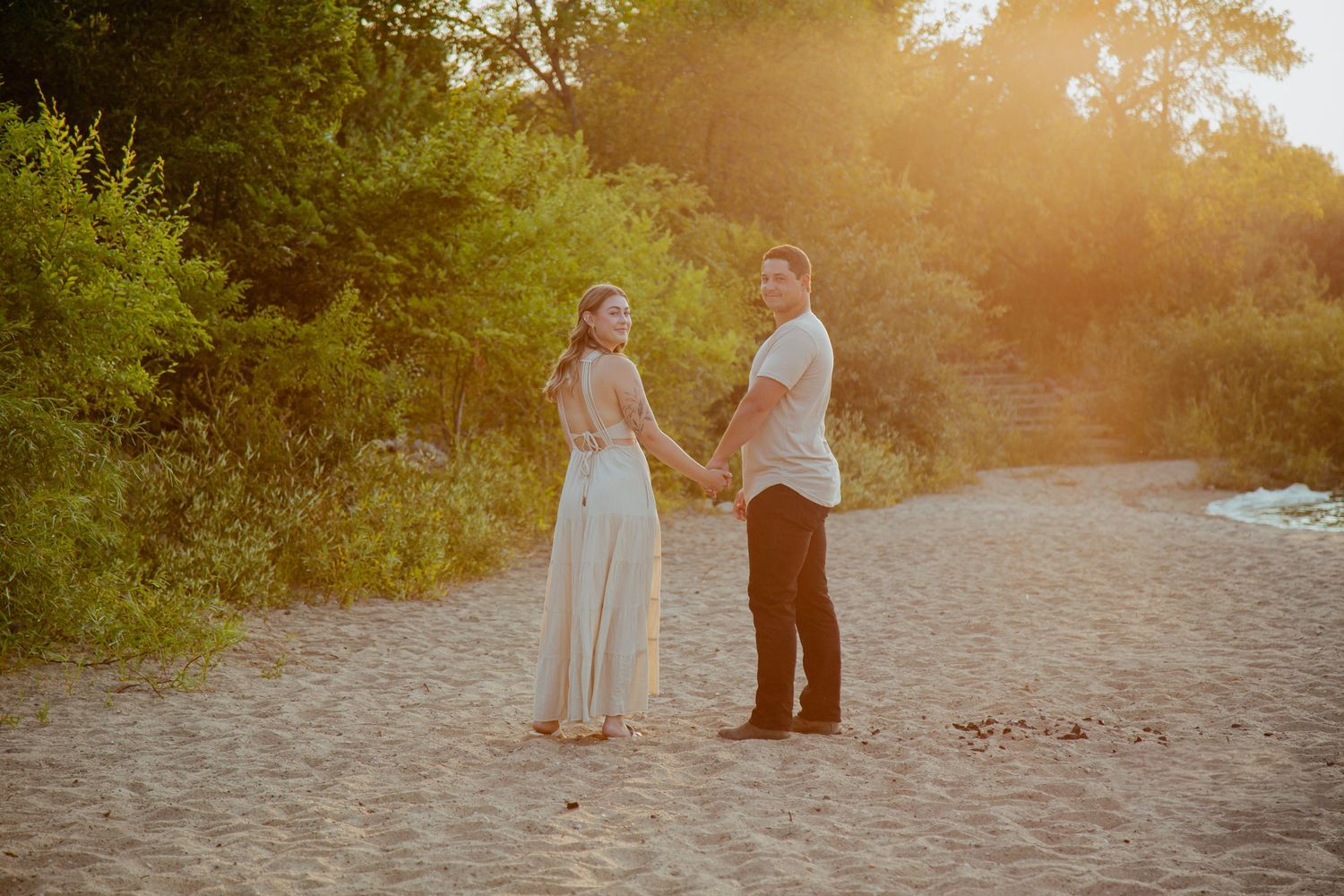 A couple stands together on a sandy path during golden hour.