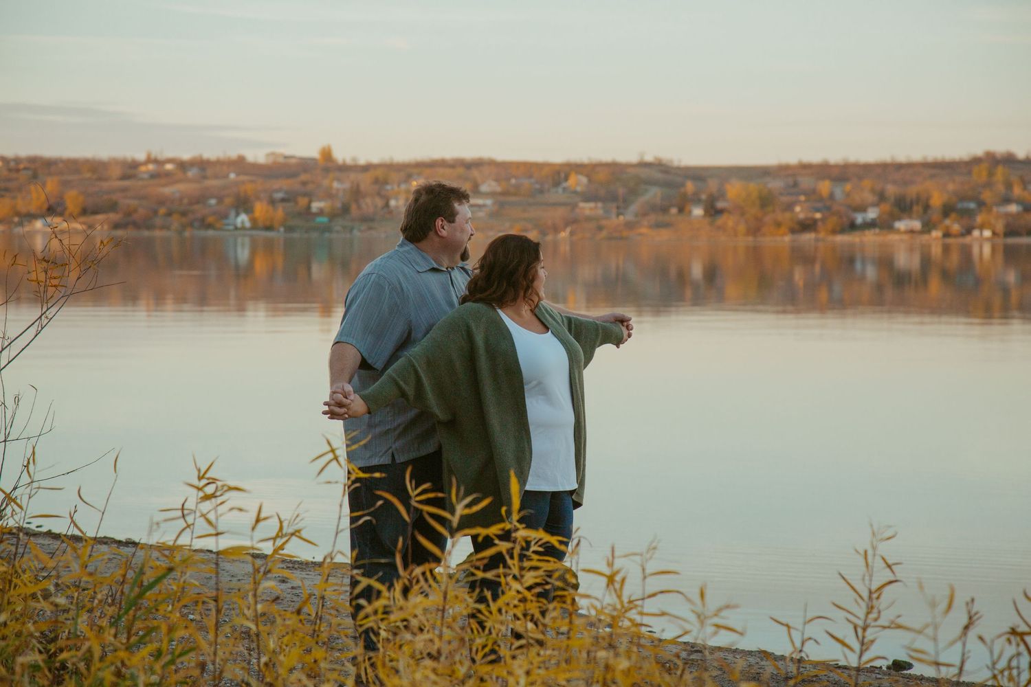 Two people standing together at golden hour overlooking a peaceful lake.