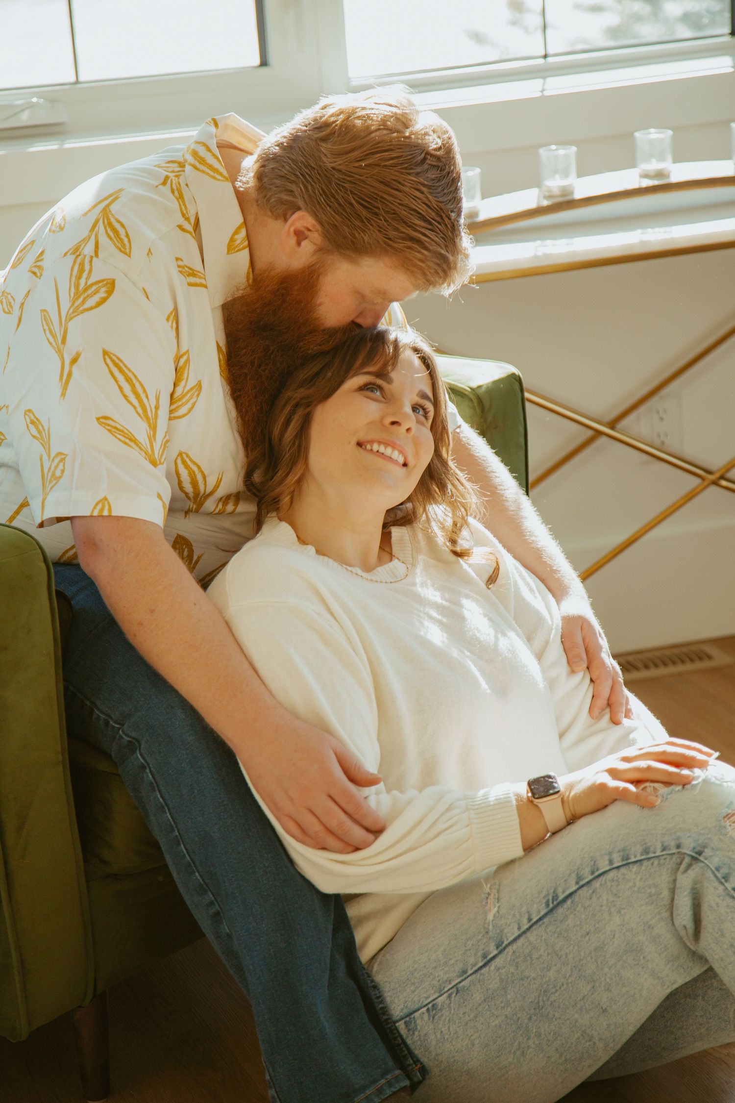 Intimate couple sharing an affectionate moment on a cozy armchair by a bright window.