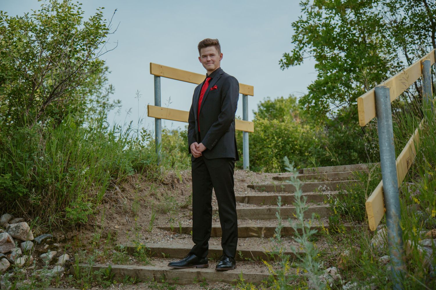 Formal portrait near wooden railing and natural outdoor setting.