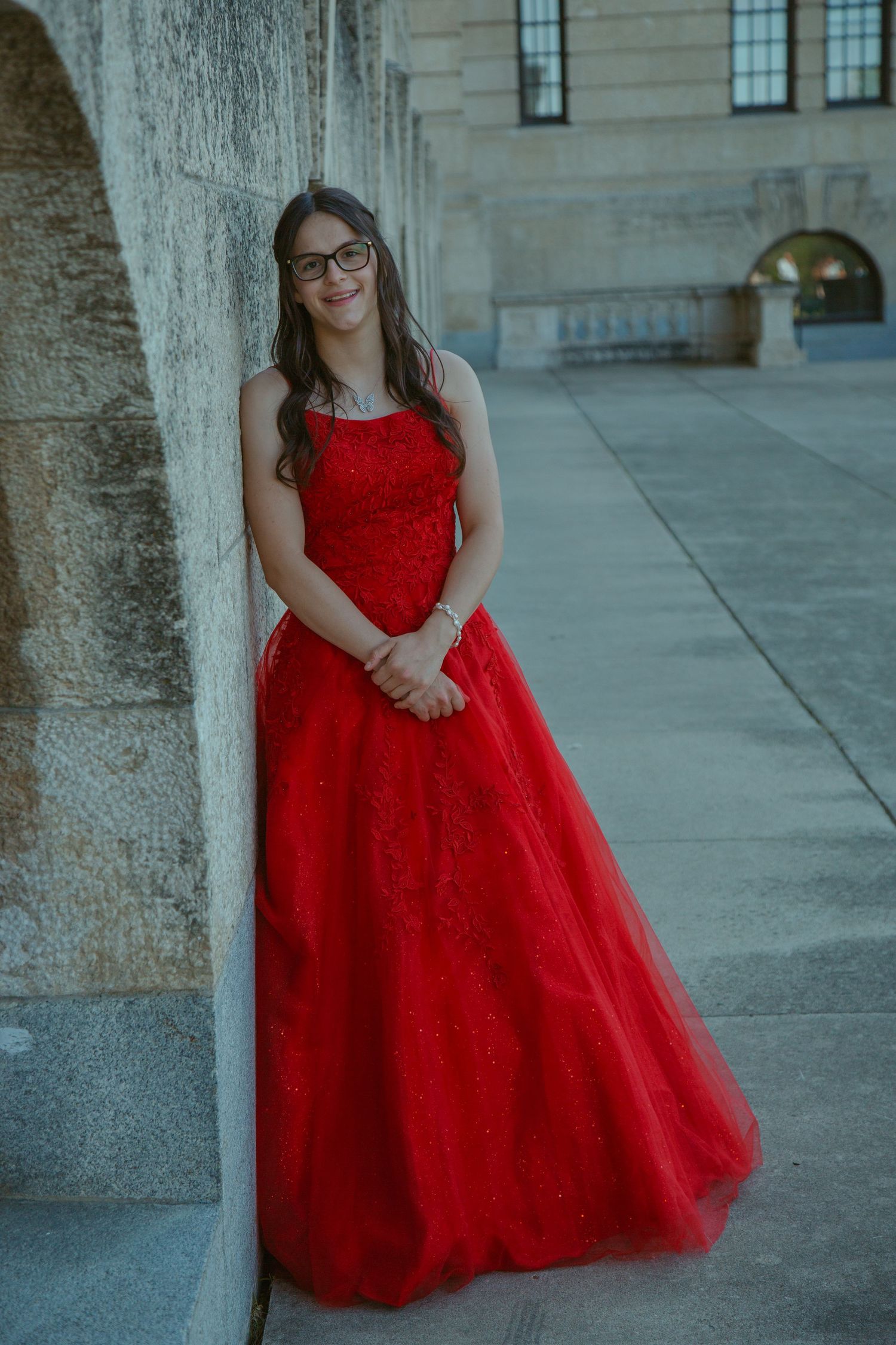 A stunning red tulle ball gown photographed against a stone building backdrop.