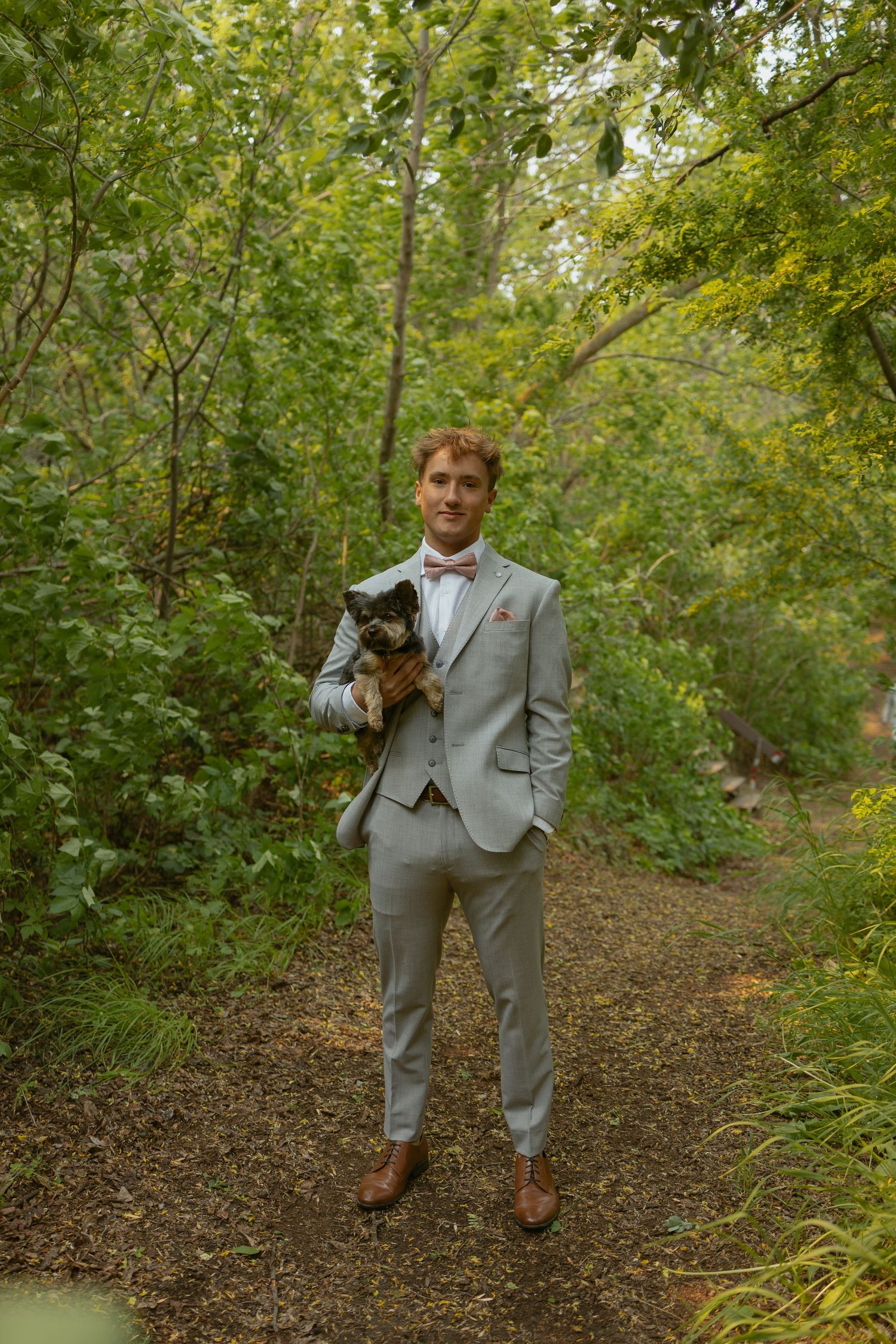 Person in light gray suit walking along a wooded trail with trees and foliage.