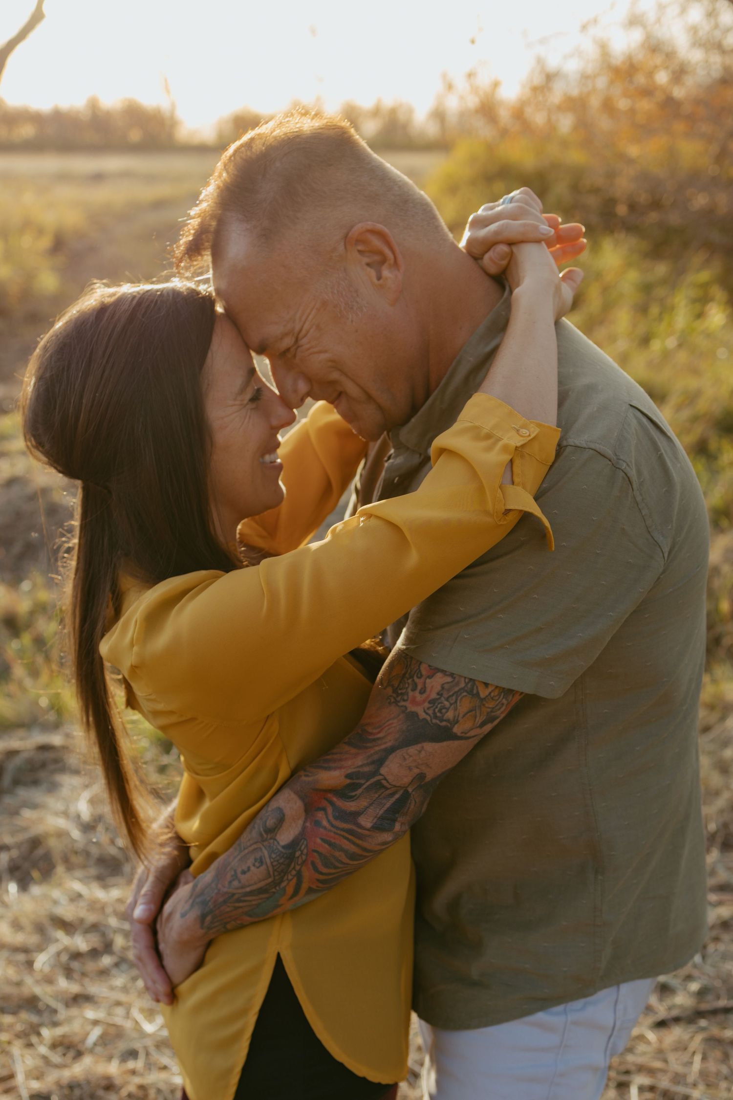 A romantic embrace captured in warm sunset lighting against a natural outdoor backdrop.