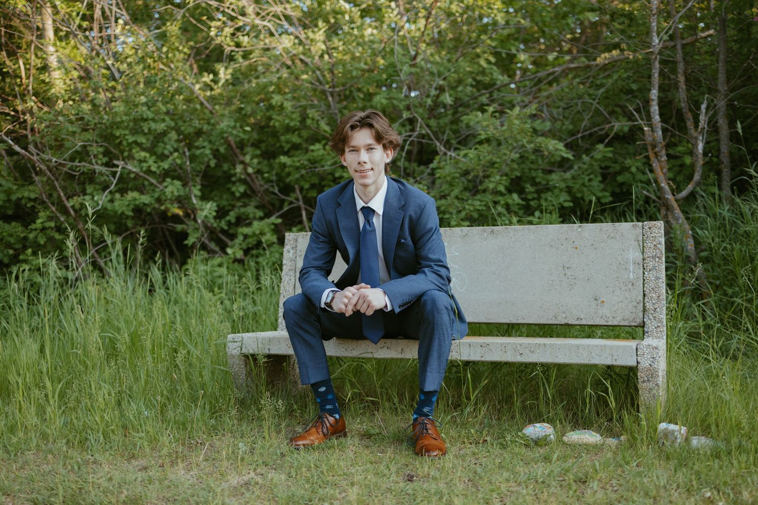 Person in blue suit sits on wooden bench in natural outdoor setting with greenery.
