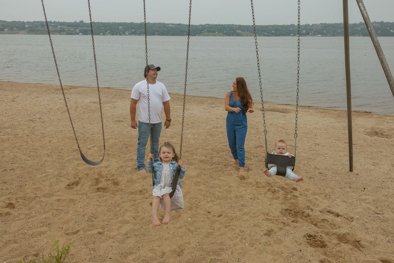 Children playing on swings at a sandy beach with water in the background.