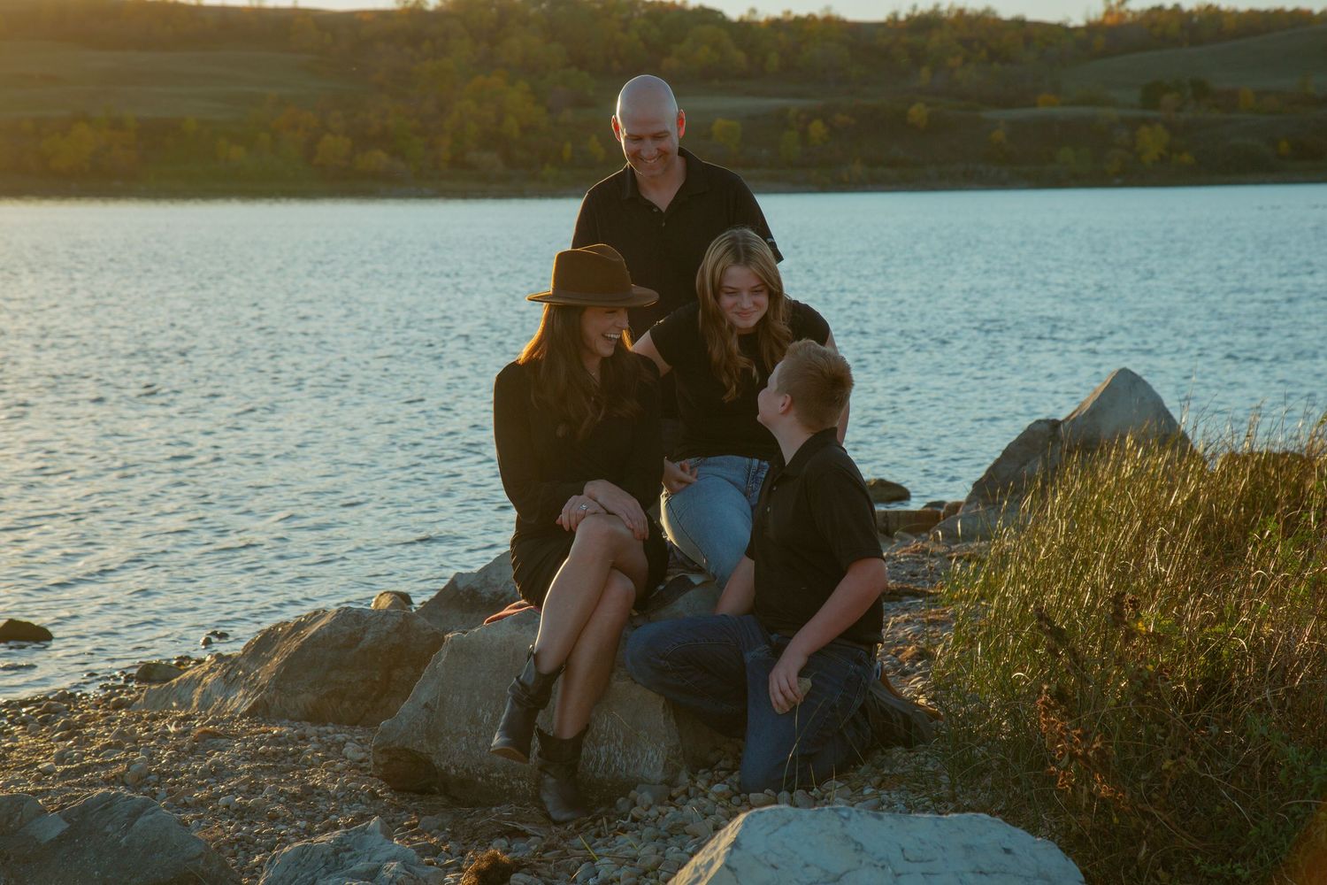 People relaxing on rocky shoreline during golden hour by the water.